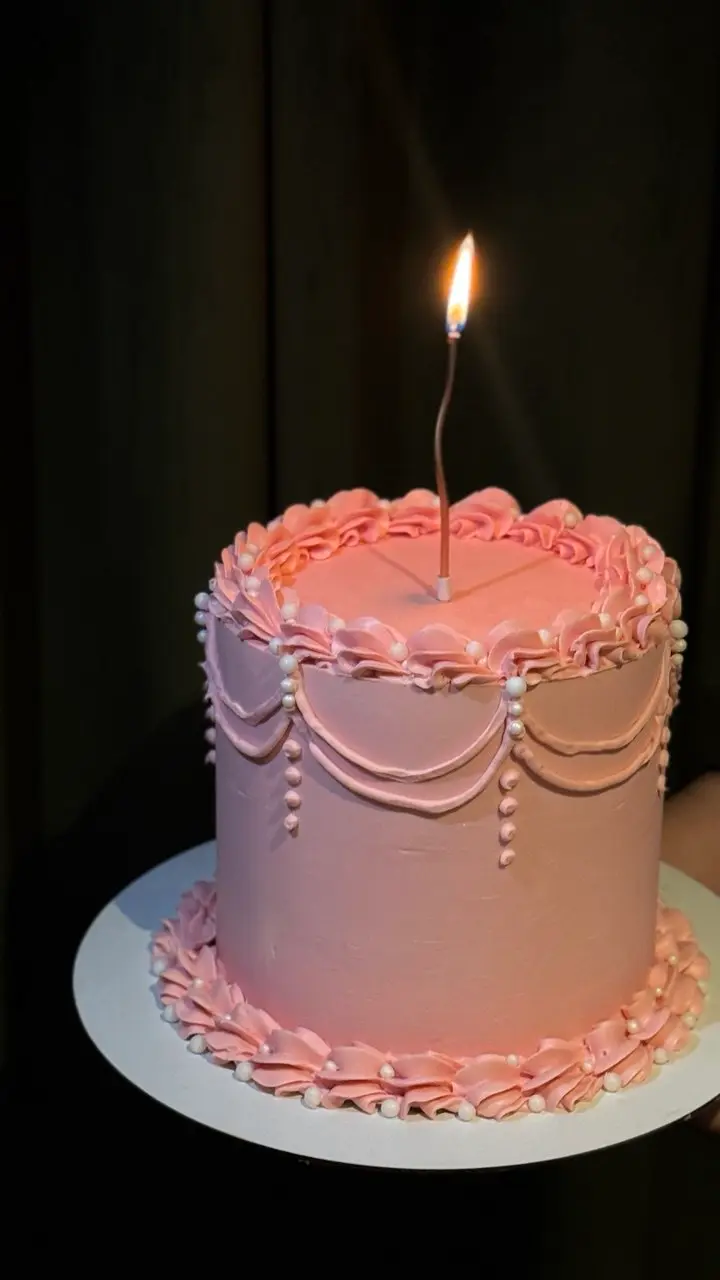 Pink and lavender ombre cake with decorative piping and single lit candle