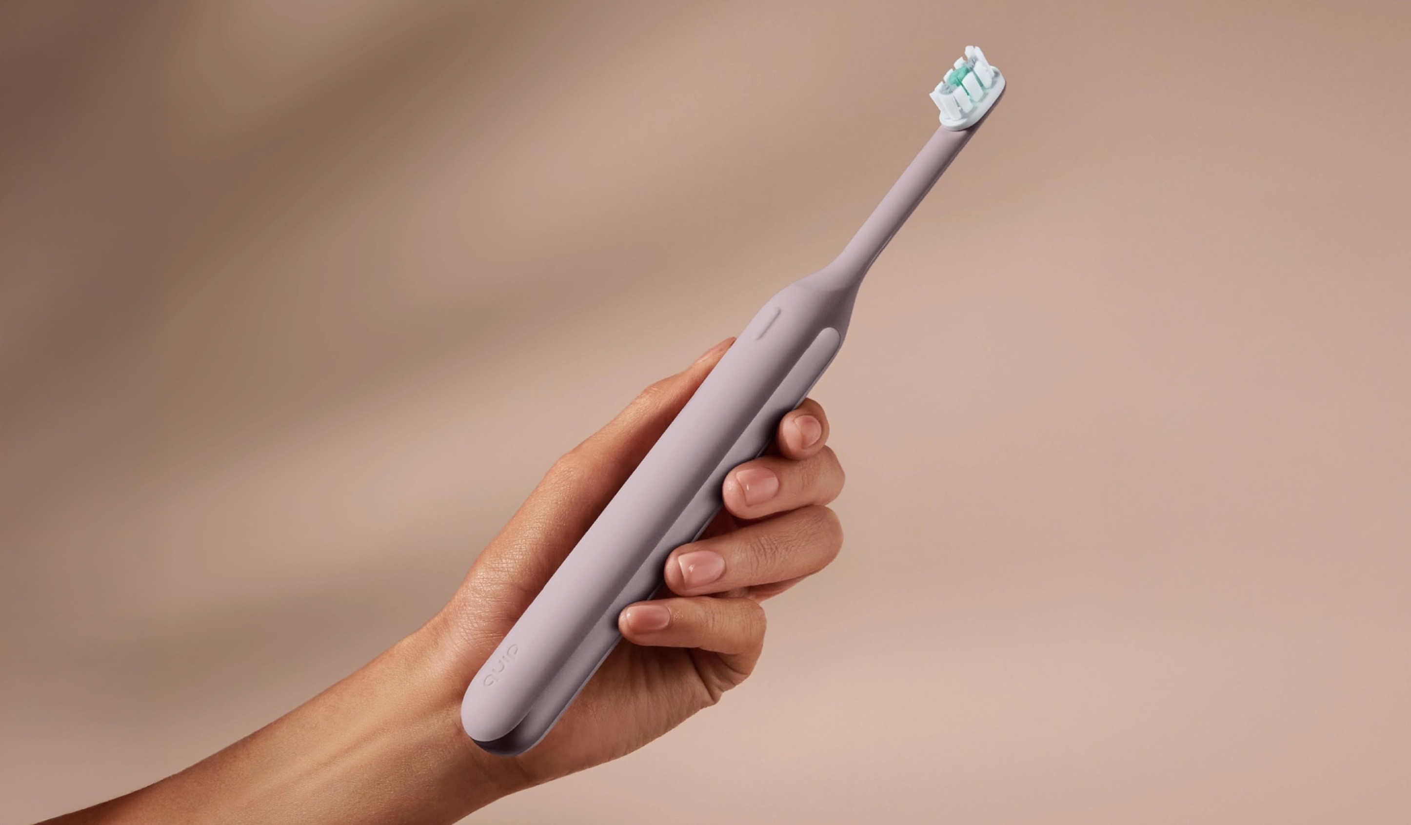 A hand holding a pink electric toothbrush with a seamless silicone body.
