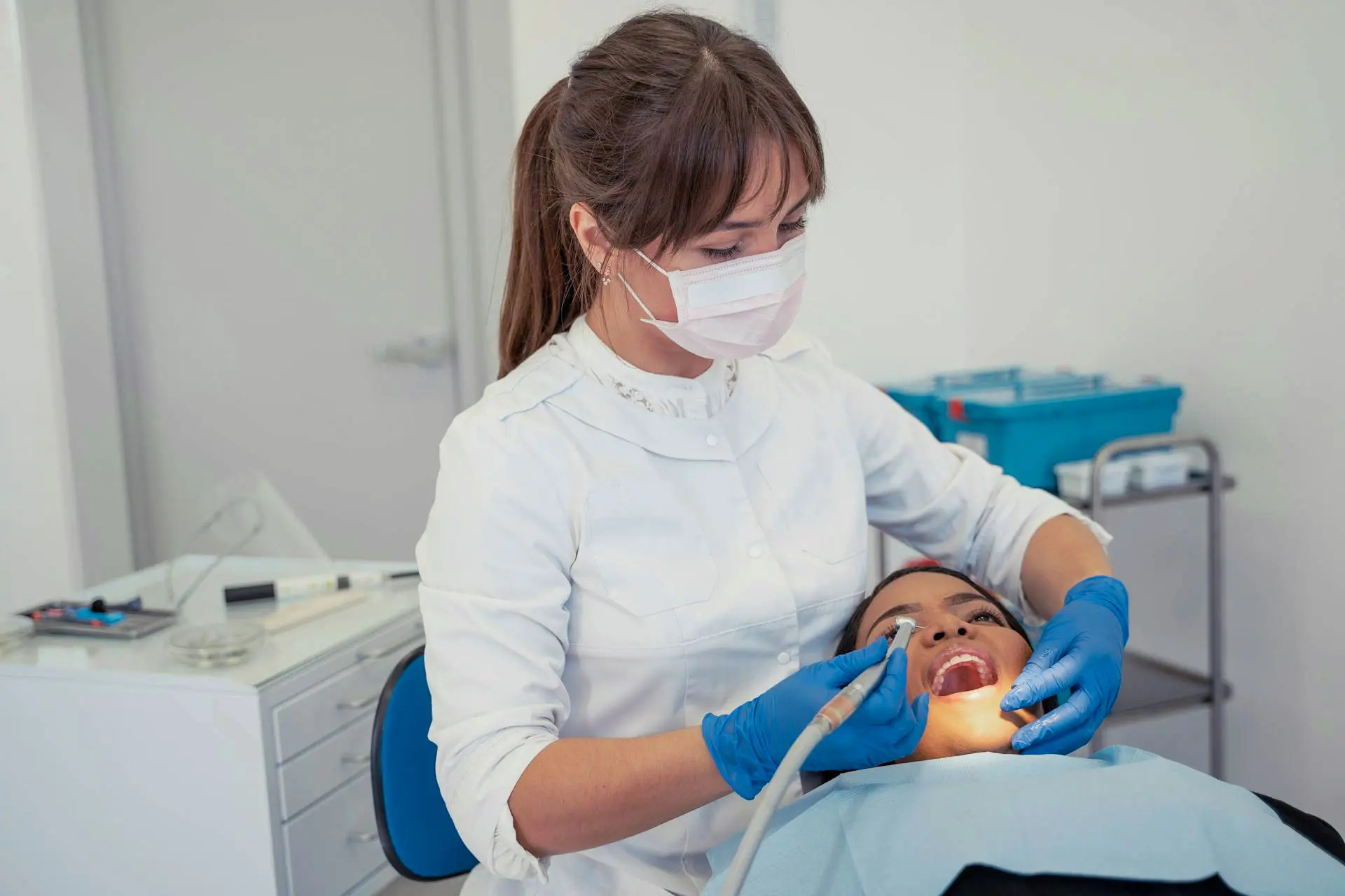 A woman in a face mask and gloves works on a patient's hand in a medical setting.