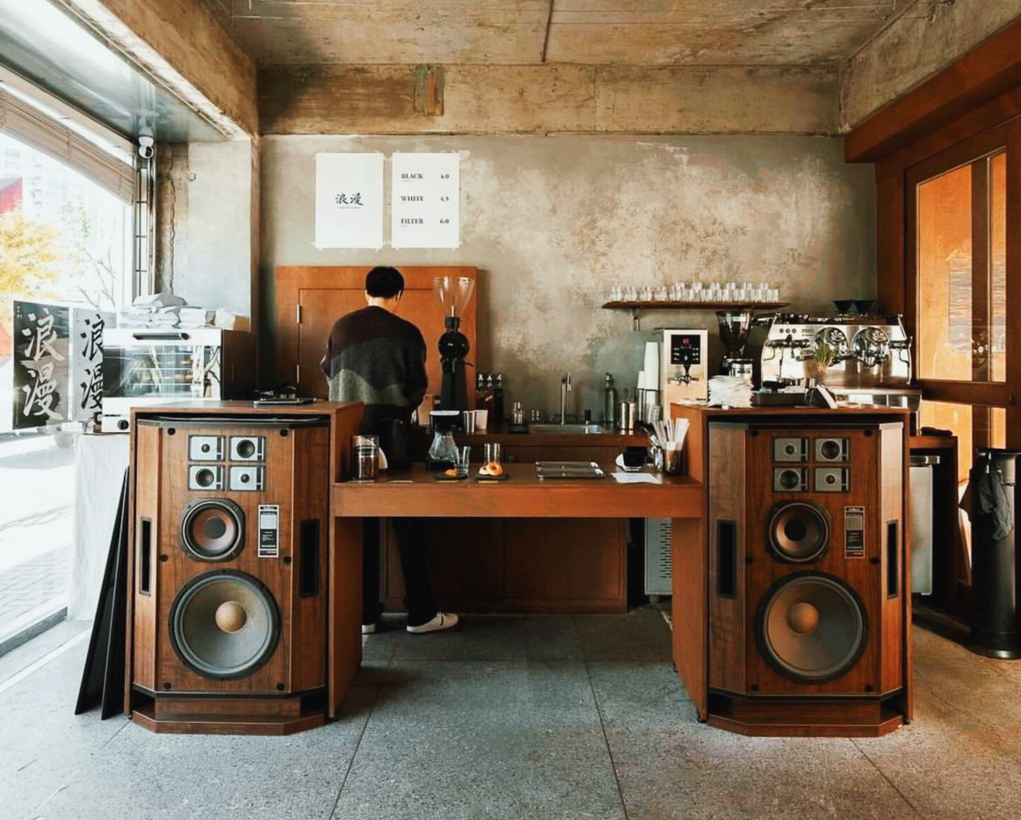 Bright record shop or cafe framed by large vintage speakers and wood cabinetry.