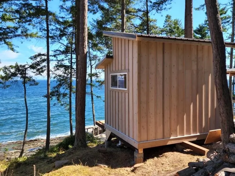 small wood cabin under construction overlooking the ocean surrounded by trees