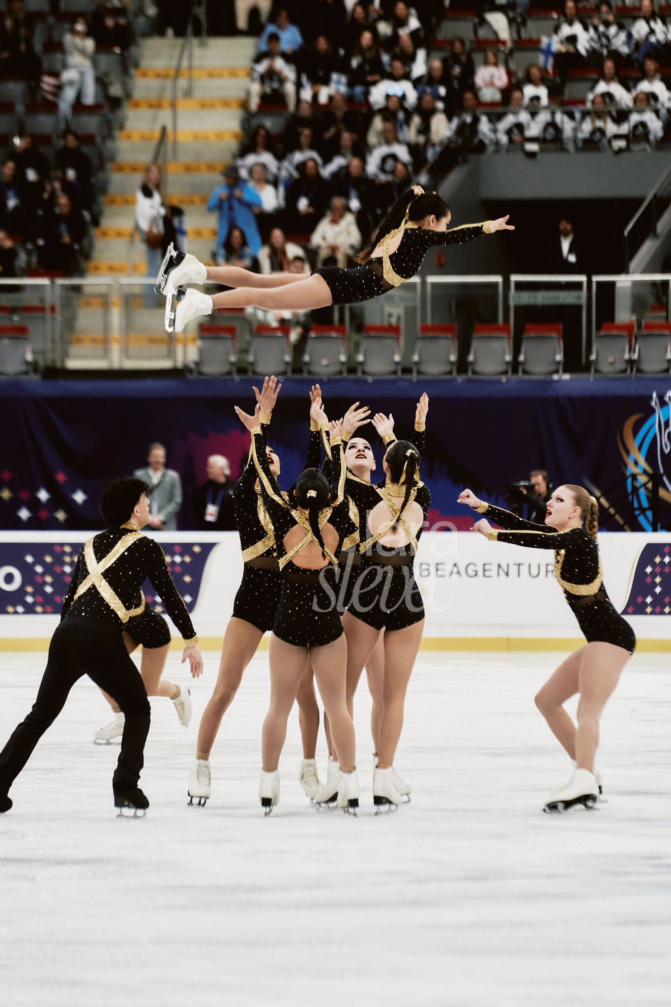 Eine Eiskunstläuferin wird von ihrem Team horizontal in die Luft geworfen. Premiere des Synchro9 bei der ISU Synchronized Skating Championships 2026 in Salzburg. Fotografiert von Lara Slevec.