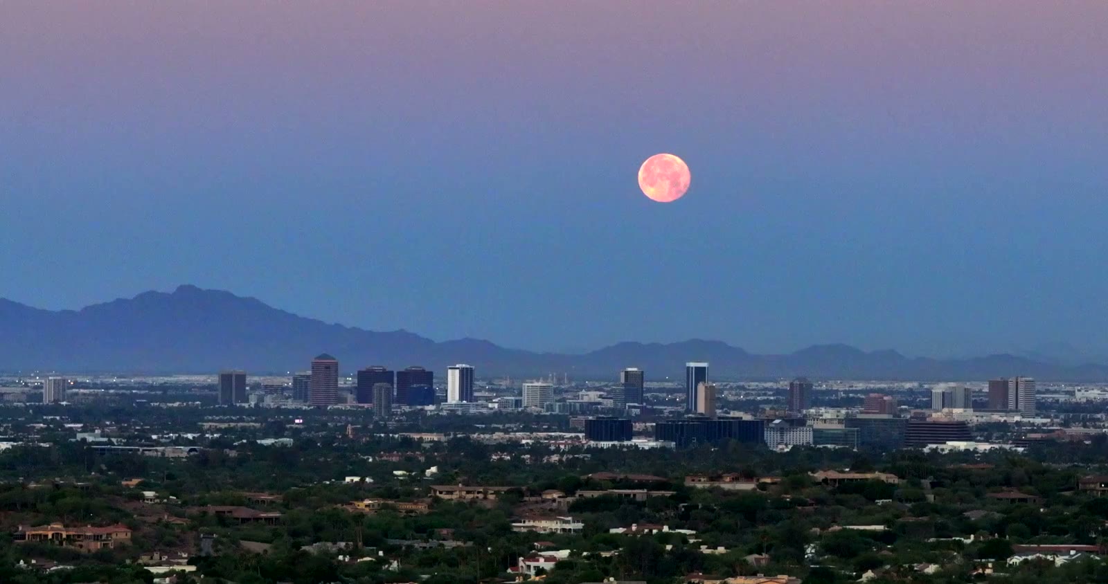 Moon rising over the city lights at dusk