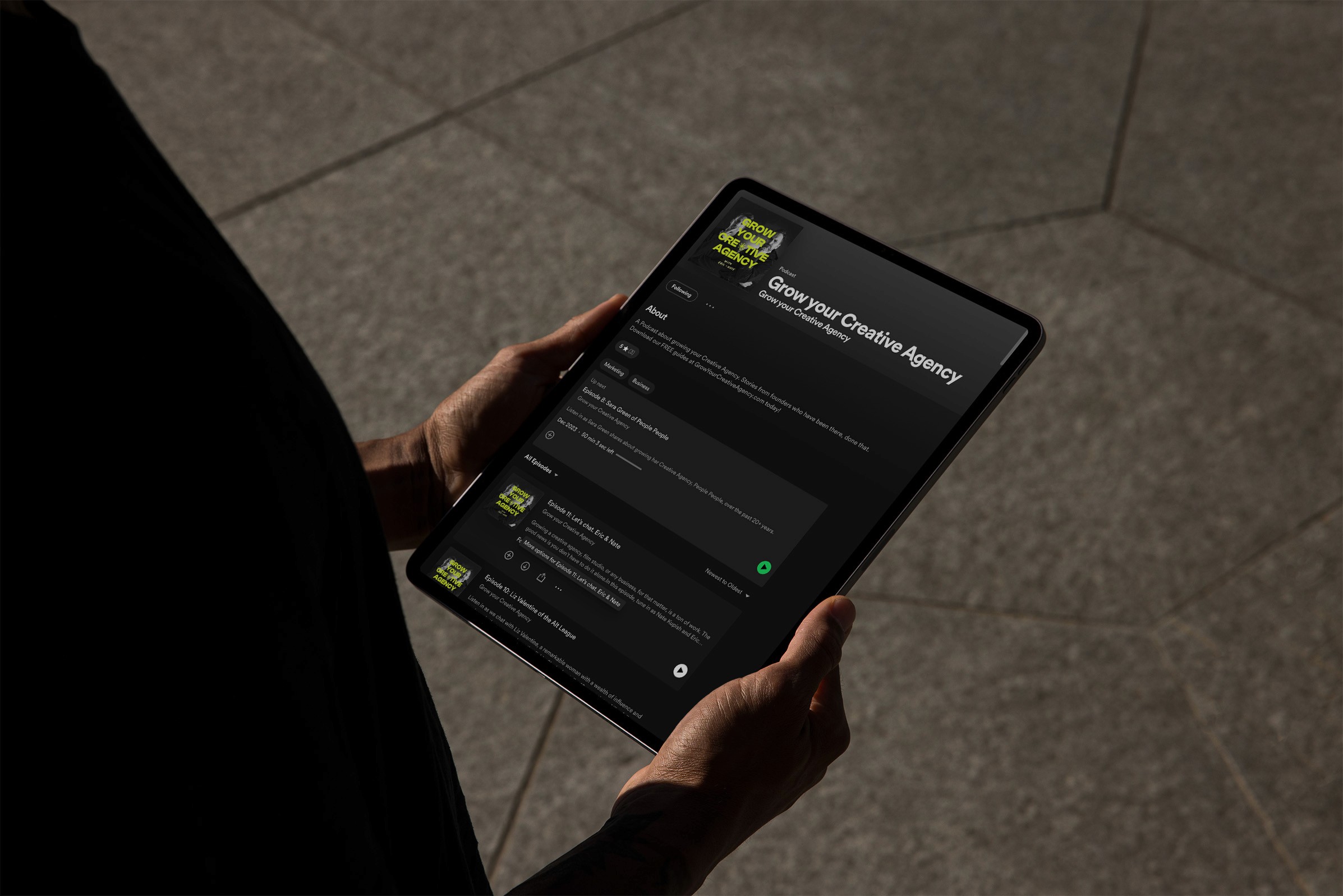 Tablet showing "Grow Your Creative Agency" podcast on Spotify. Hands holding device.