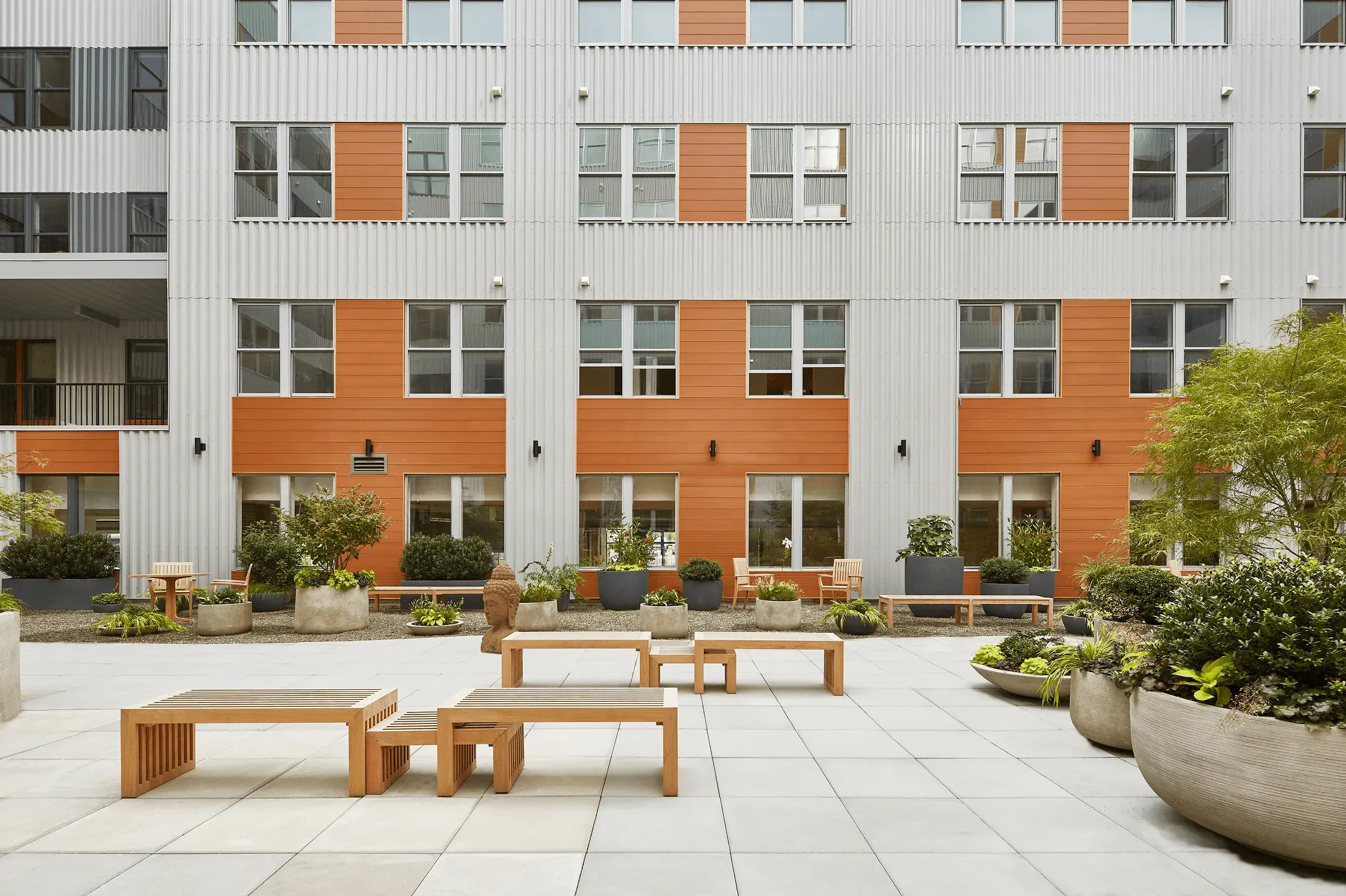 Modern apartment building exterior with rows of windows and a landscaped courtyard featuring seating areas.