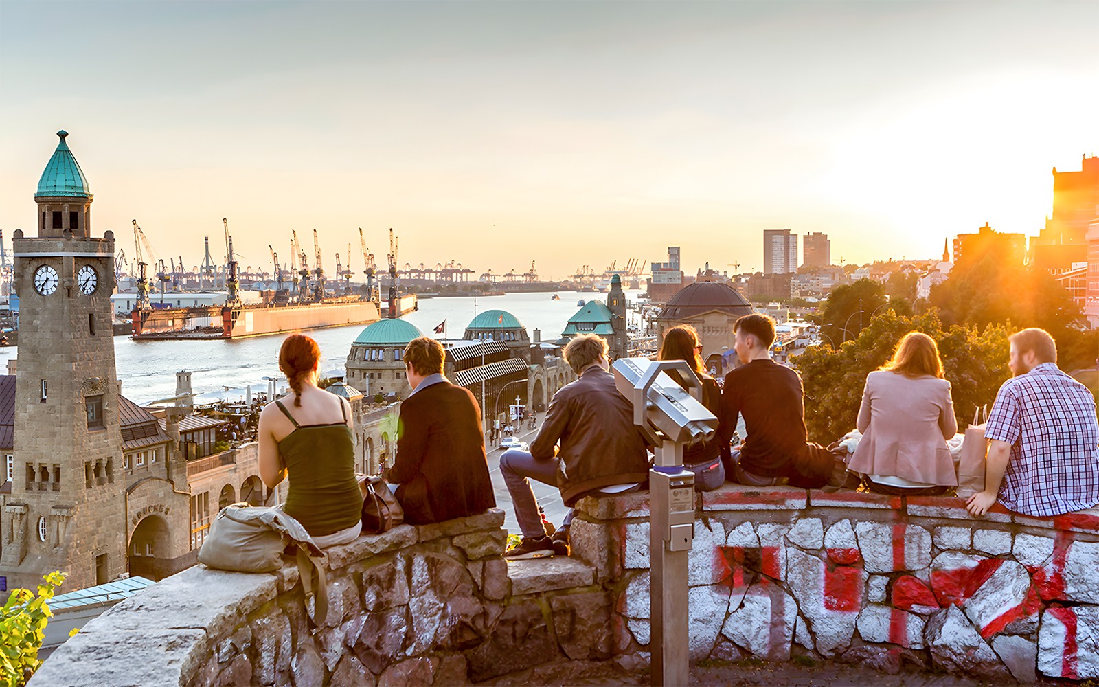 People enjoying sunset view of Hamburg harbor with clock tower and Elbe River.