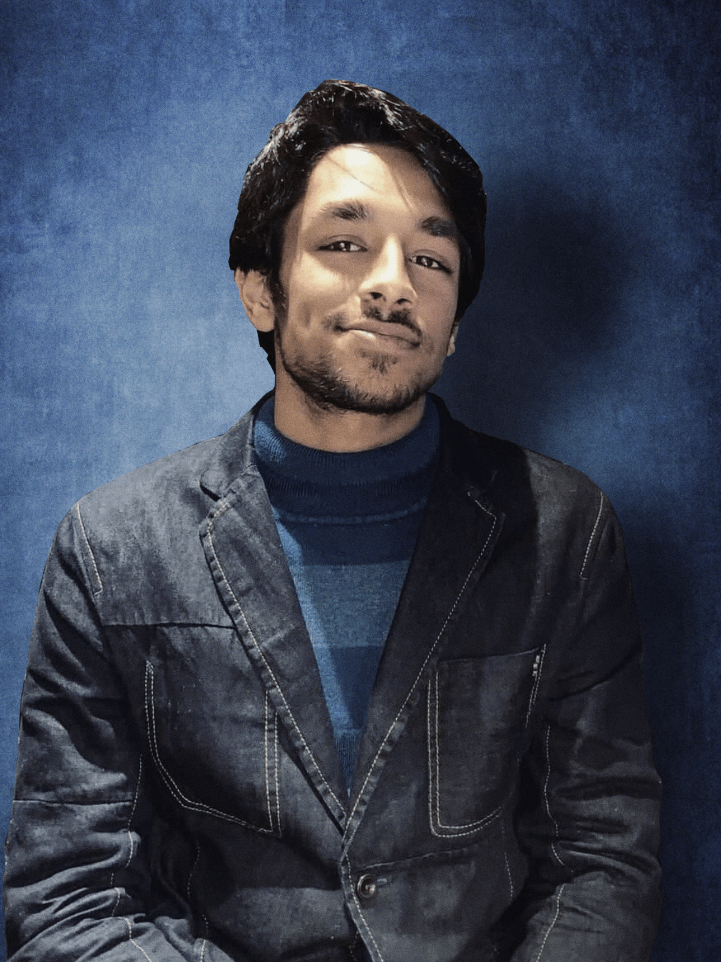 Smiling young man with curly hair, wearing a dark hoodie, against a softly lit background.
