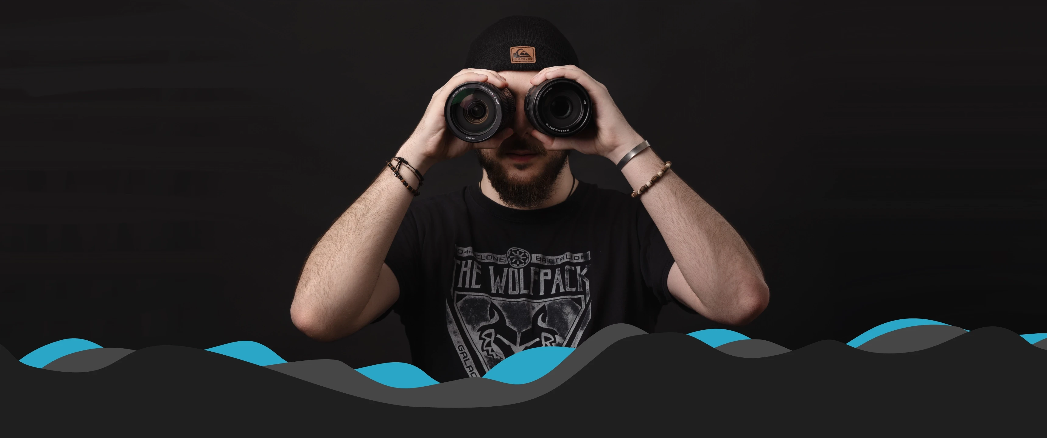 Videographer holding two camera lenses to eyes against a dark background, symbolising creative vision, professional videography services and content production by Raybrand Media