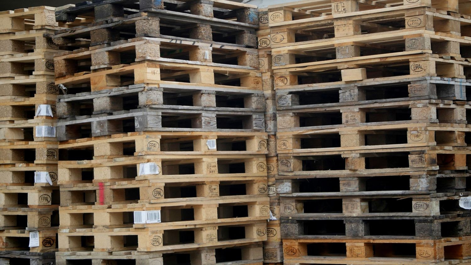 Stacks of wooden pallets arranged in rows, featuring weathered textures and various shades of brown.