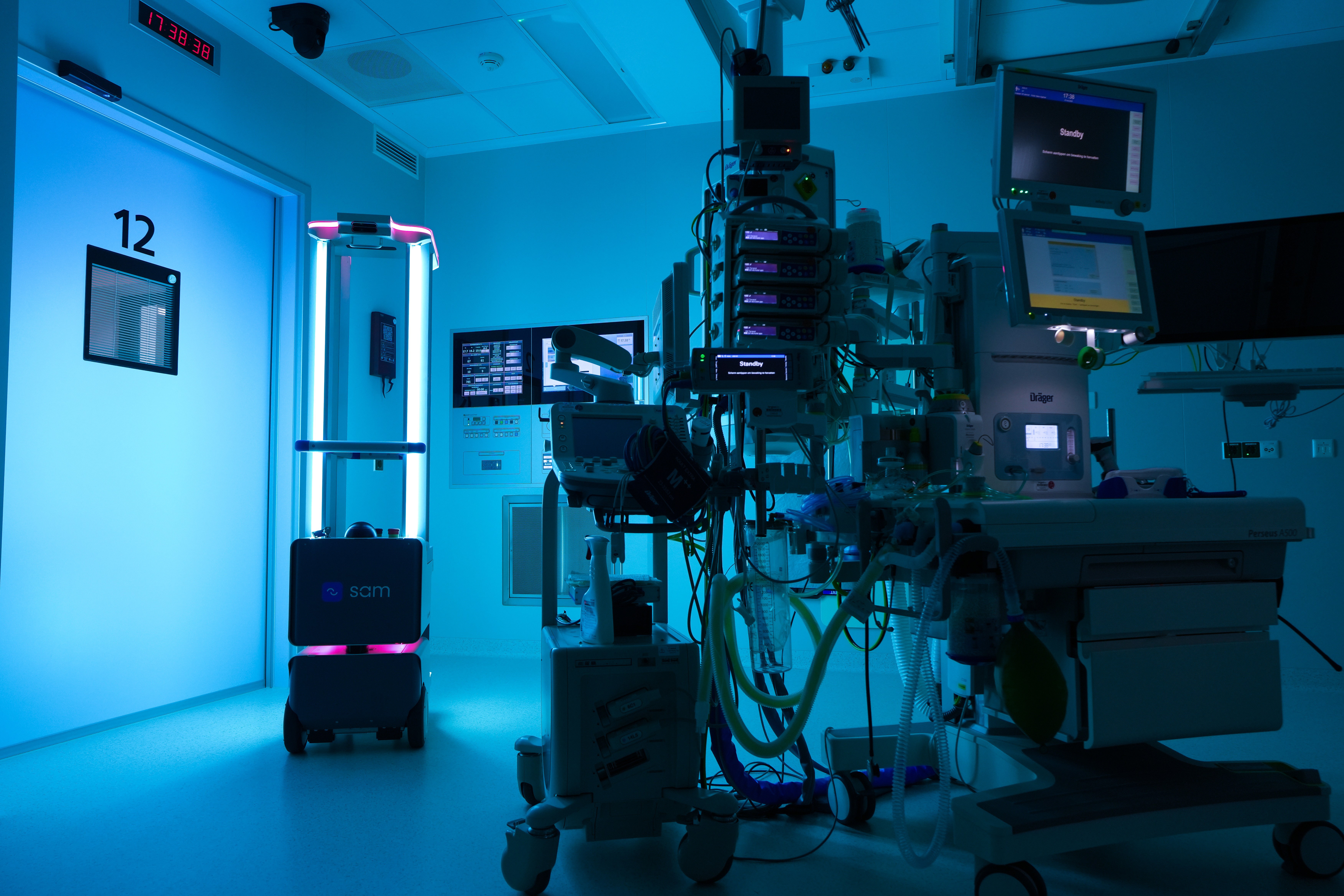The SAM® UV-C disinfection robot operates in an operating room, emitting blue light while disinfecting the space alongside anesthesia and monitoring equipment.