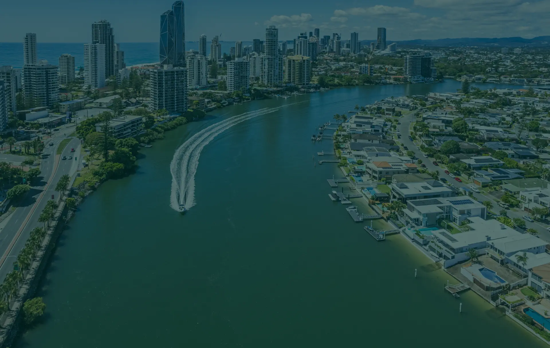Aerial view of a river with a ski boat, houses, and cityscape.