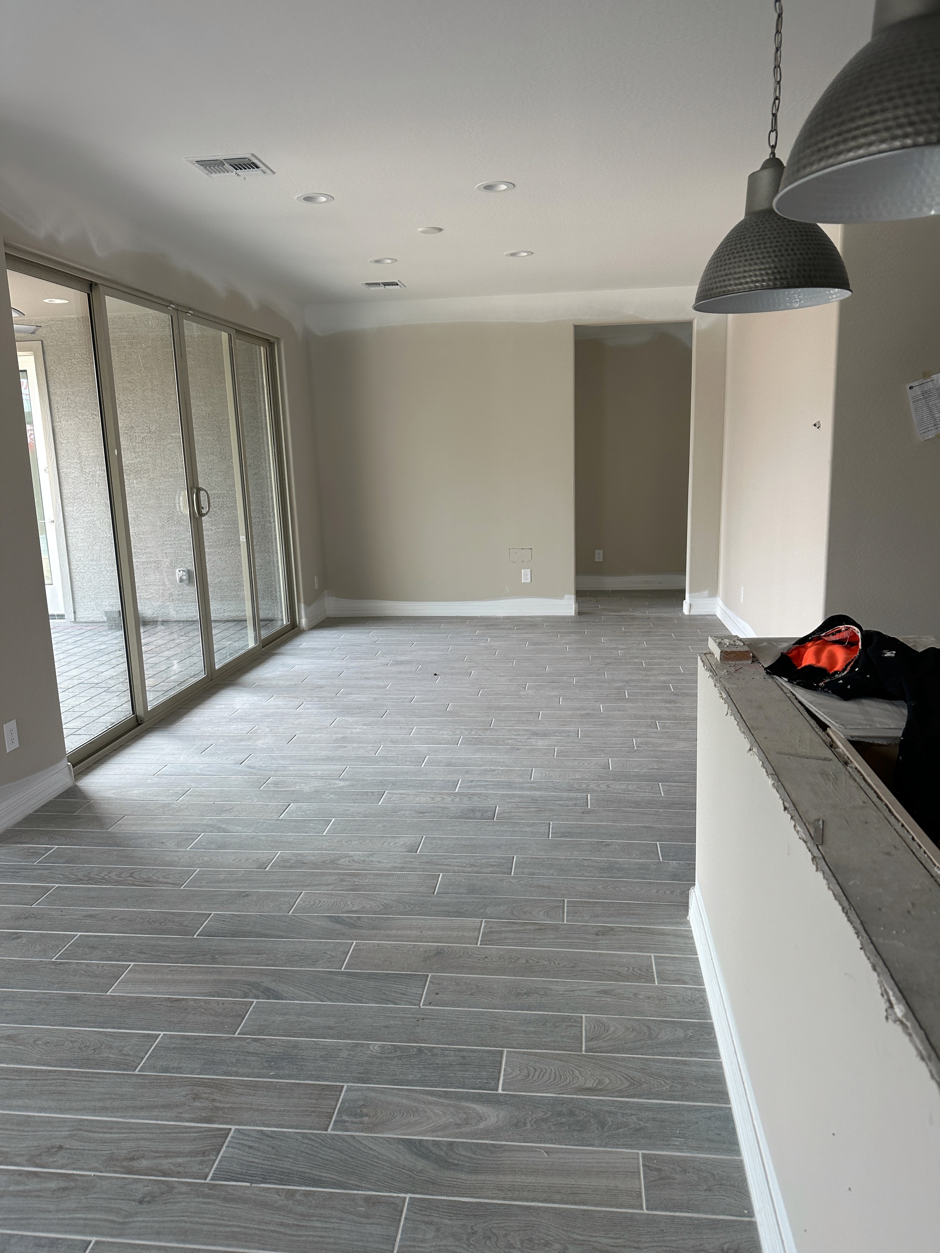 Modern living area with gray wood-look tile flooring, large sliding glass doors, and open space in a new home under construction.