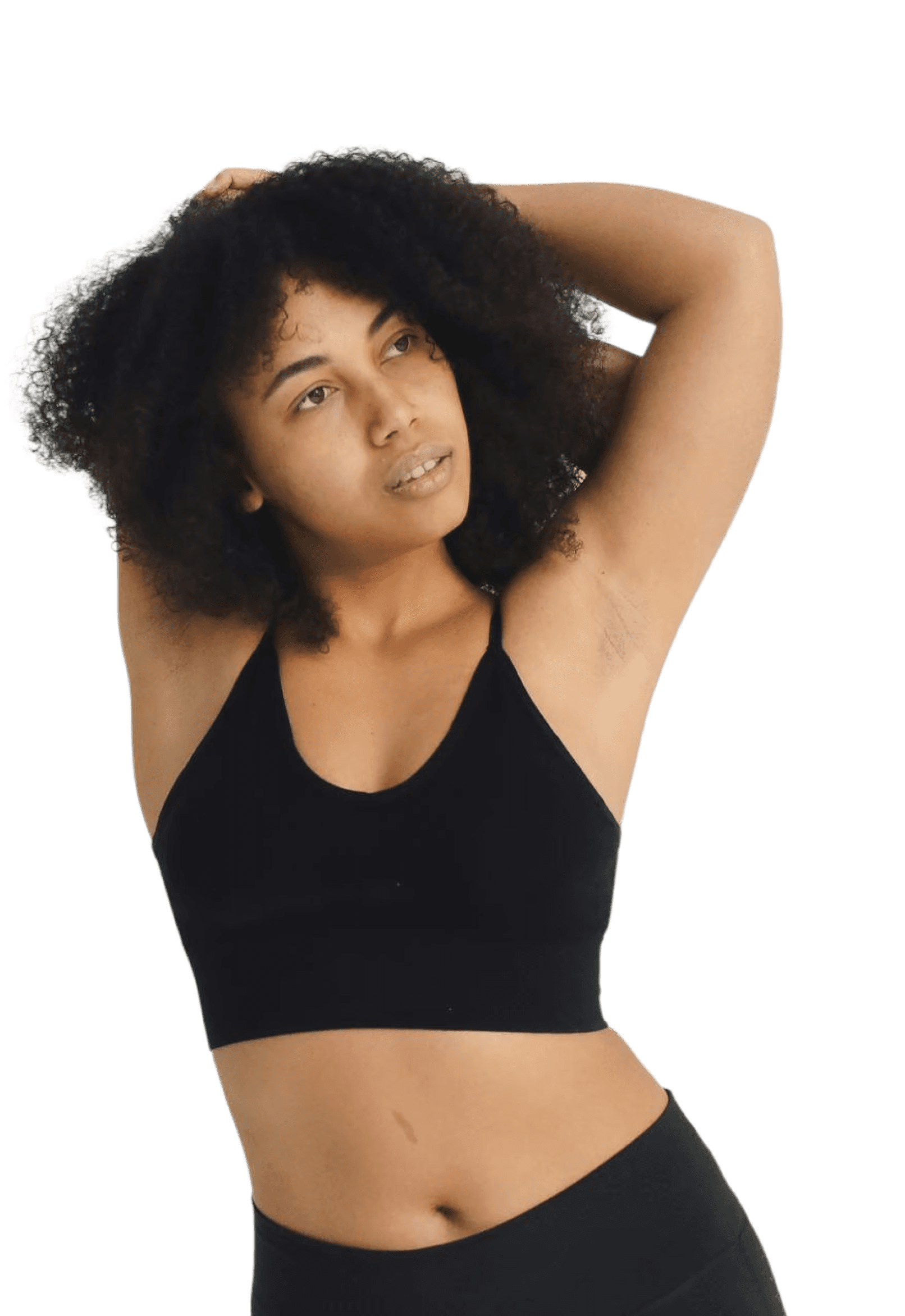 Woman with curly hair in a black sports bra poses with arms behind head, looking to the side.