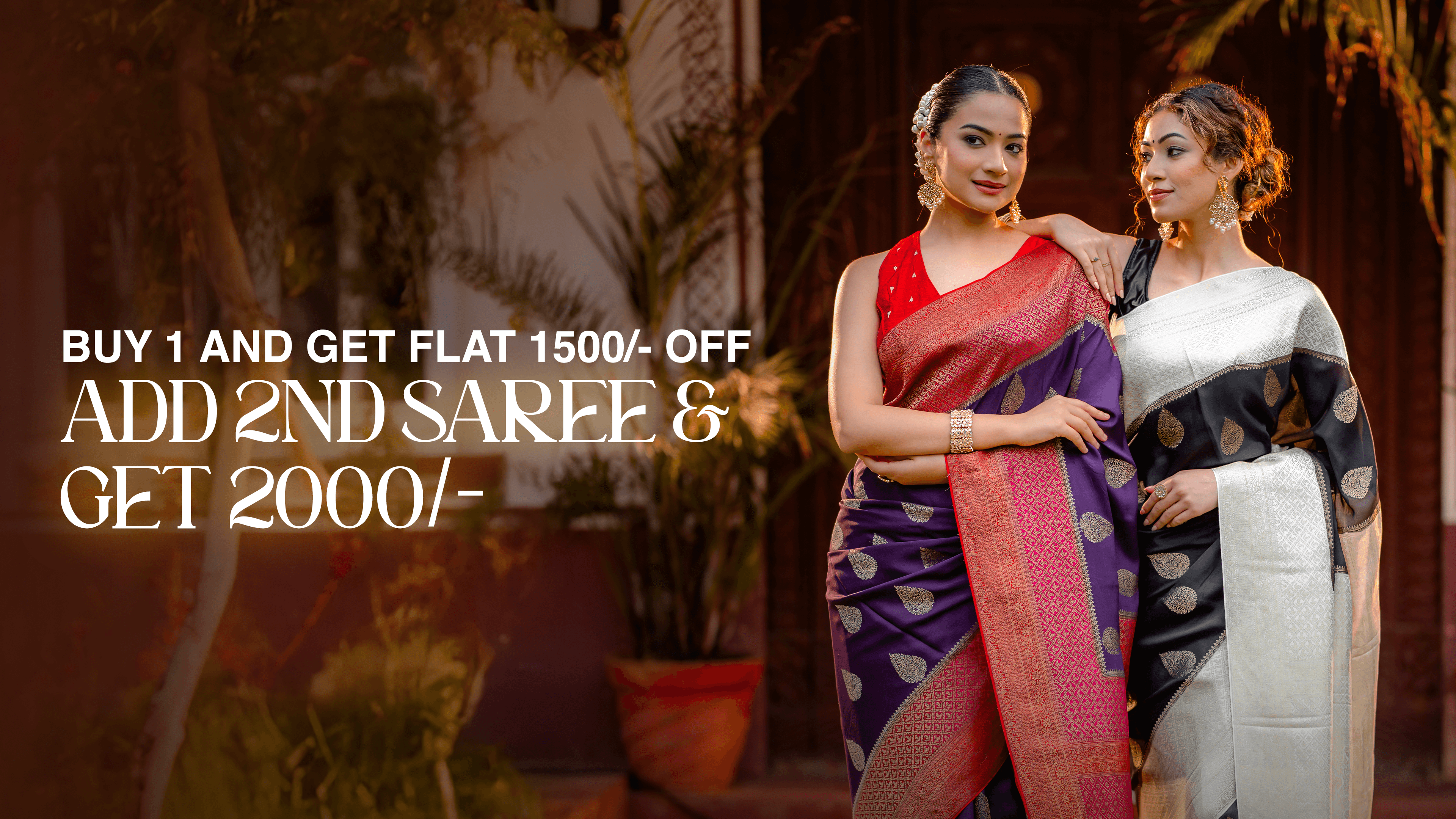 Two women standing together—one wearing a purple crepe silk saree with a pink-red contrast border and zari buttas, and the other wearing a black and white crepe saree—showcasing elegant handcrafted designs from That Saree Shop.