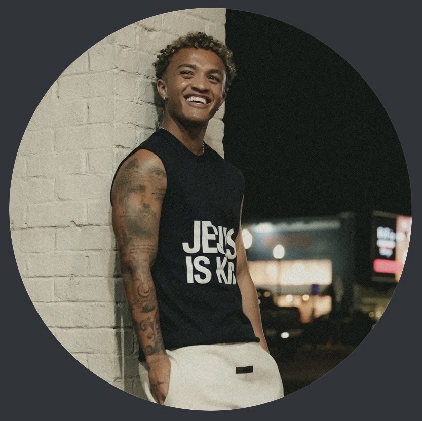 A woman with shoulder-length brown hair and freckles smiles softly. She wears a beige blazer over a white shirt in a warmly lit room, conveying professionalism and warmth.