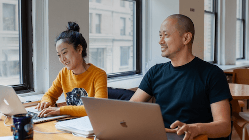 A woman and a man working side-by-side at an open workspace together.