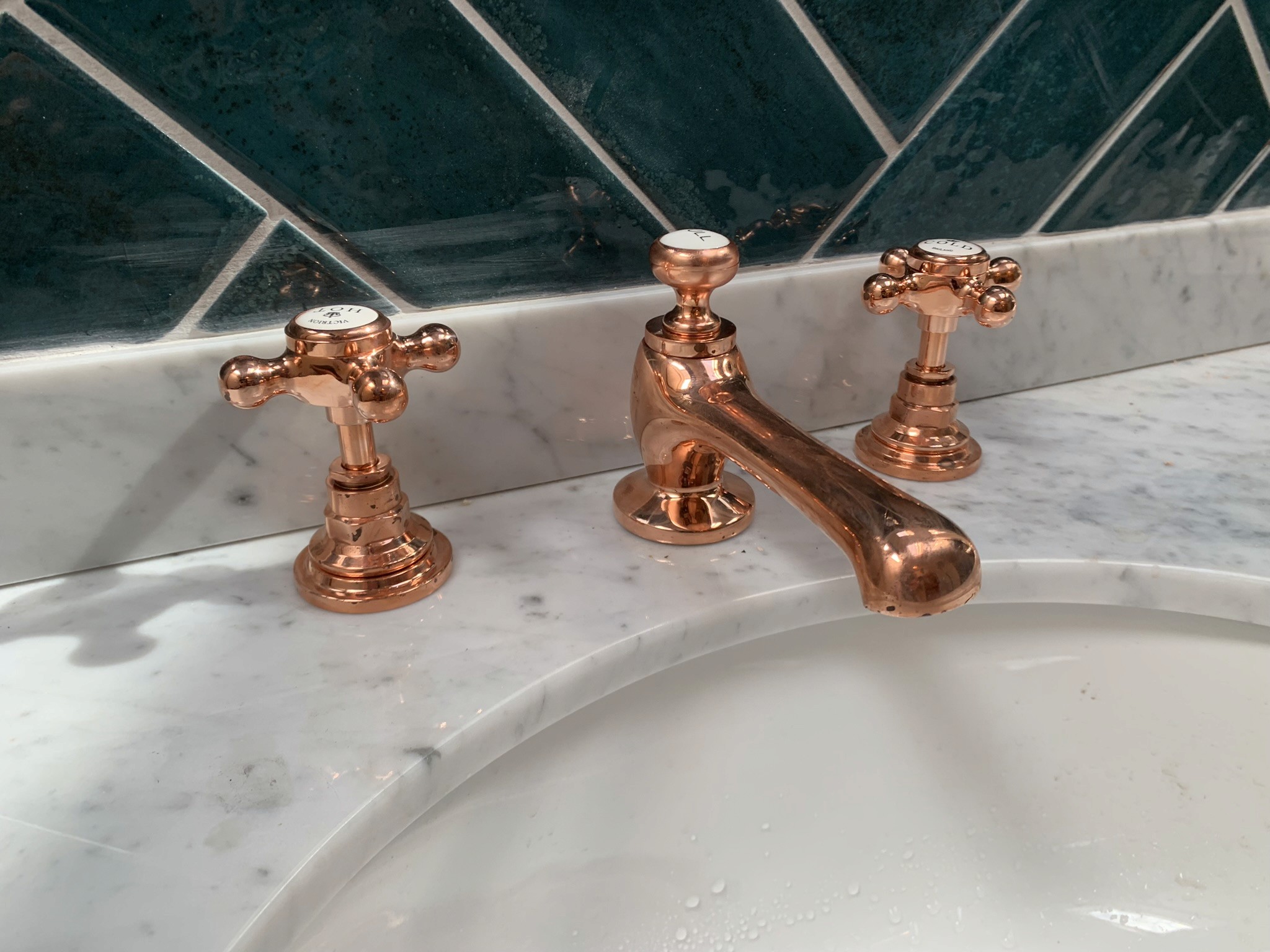 Copper taps over marble sink with green herringbone tiles