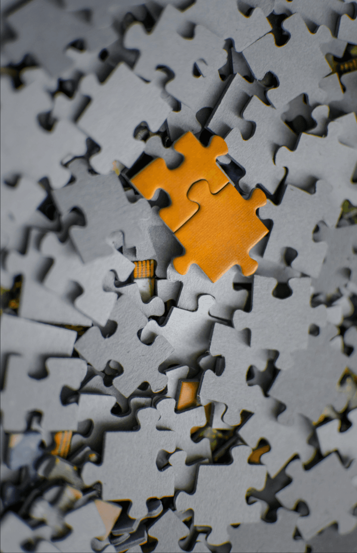 A single orange puzzle piece rests on a pile of grey pieces.