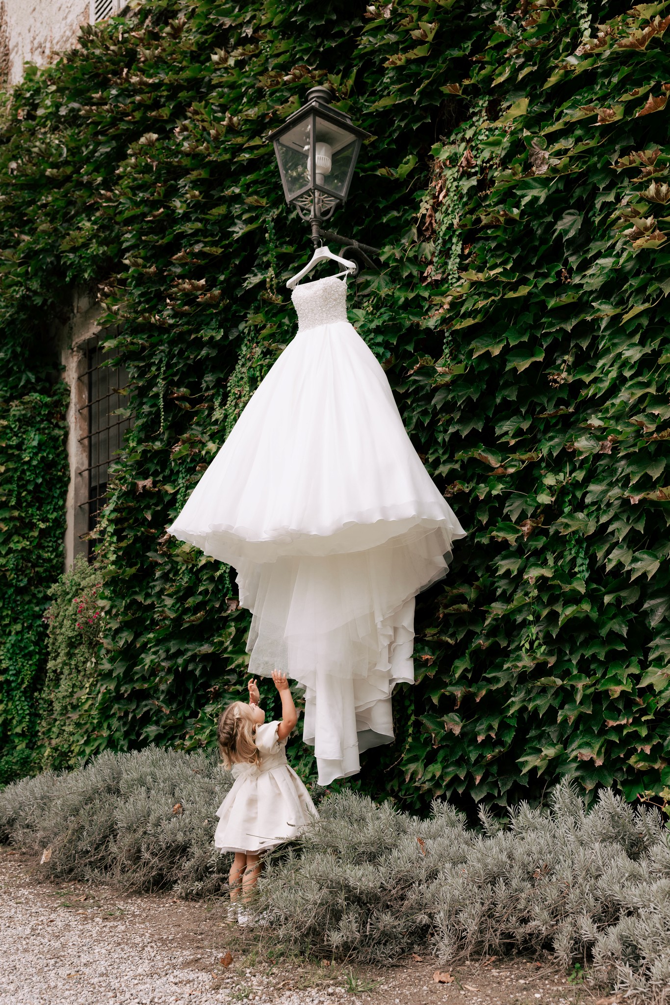 Abito da sposa appeso tra l'edera di Villa Ferrari, una bambina lo osserva con meraviglia durante i preparativi matrimoniali