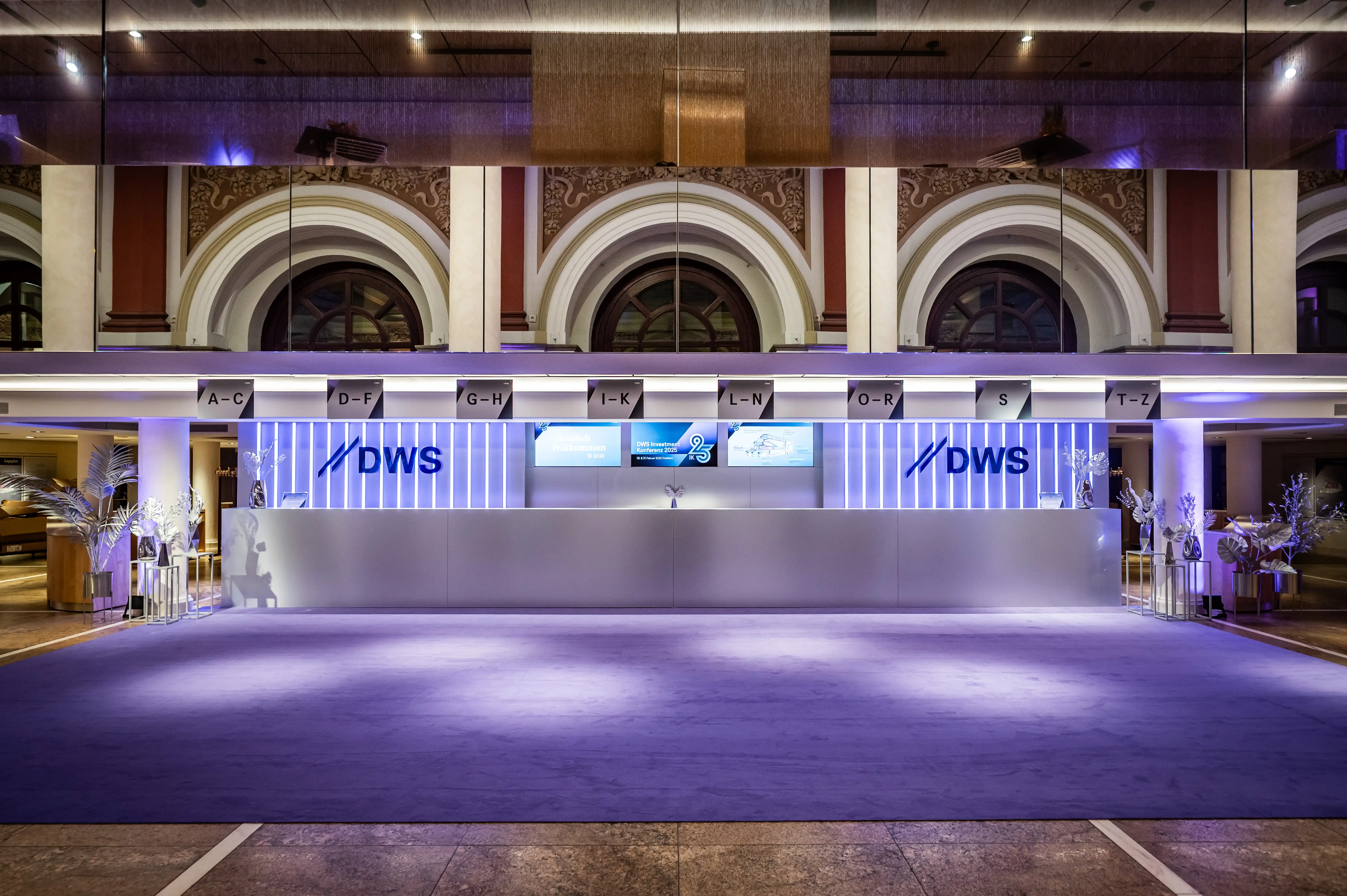 Long white DWS check-in counter with light strips and alphabet signs in a historic hall.