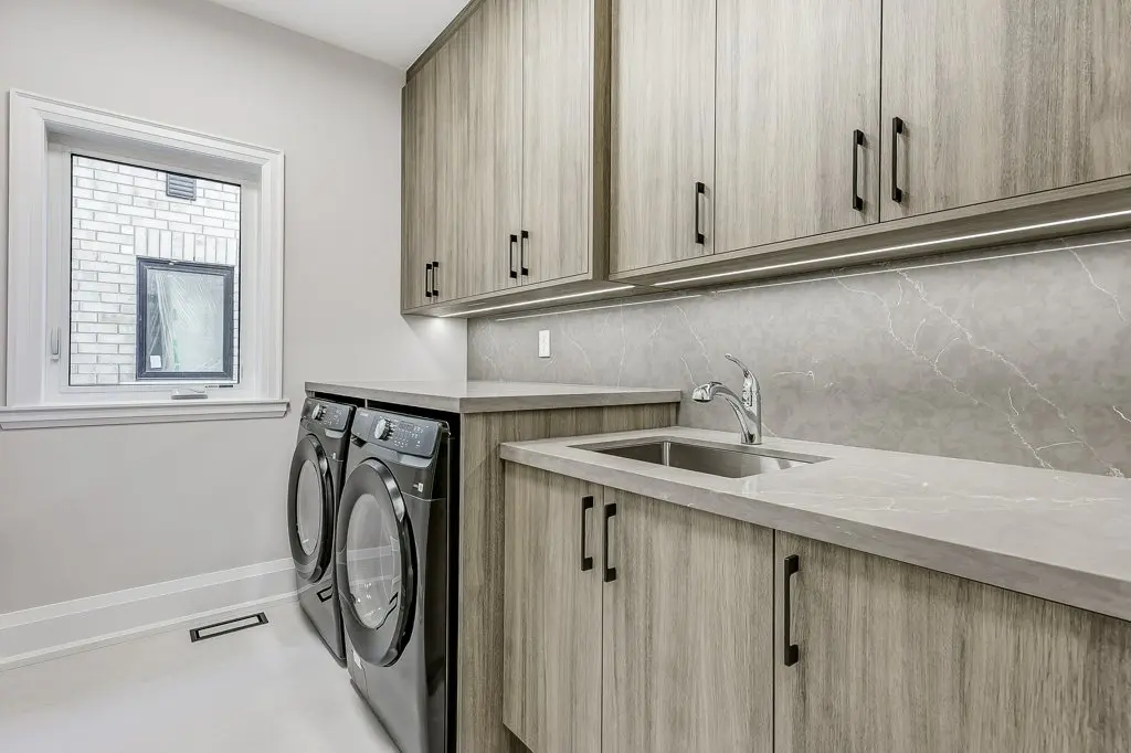 Photo of second floor laundry room with side by side machines, stone counter, and undermount sink, including lots of storage.