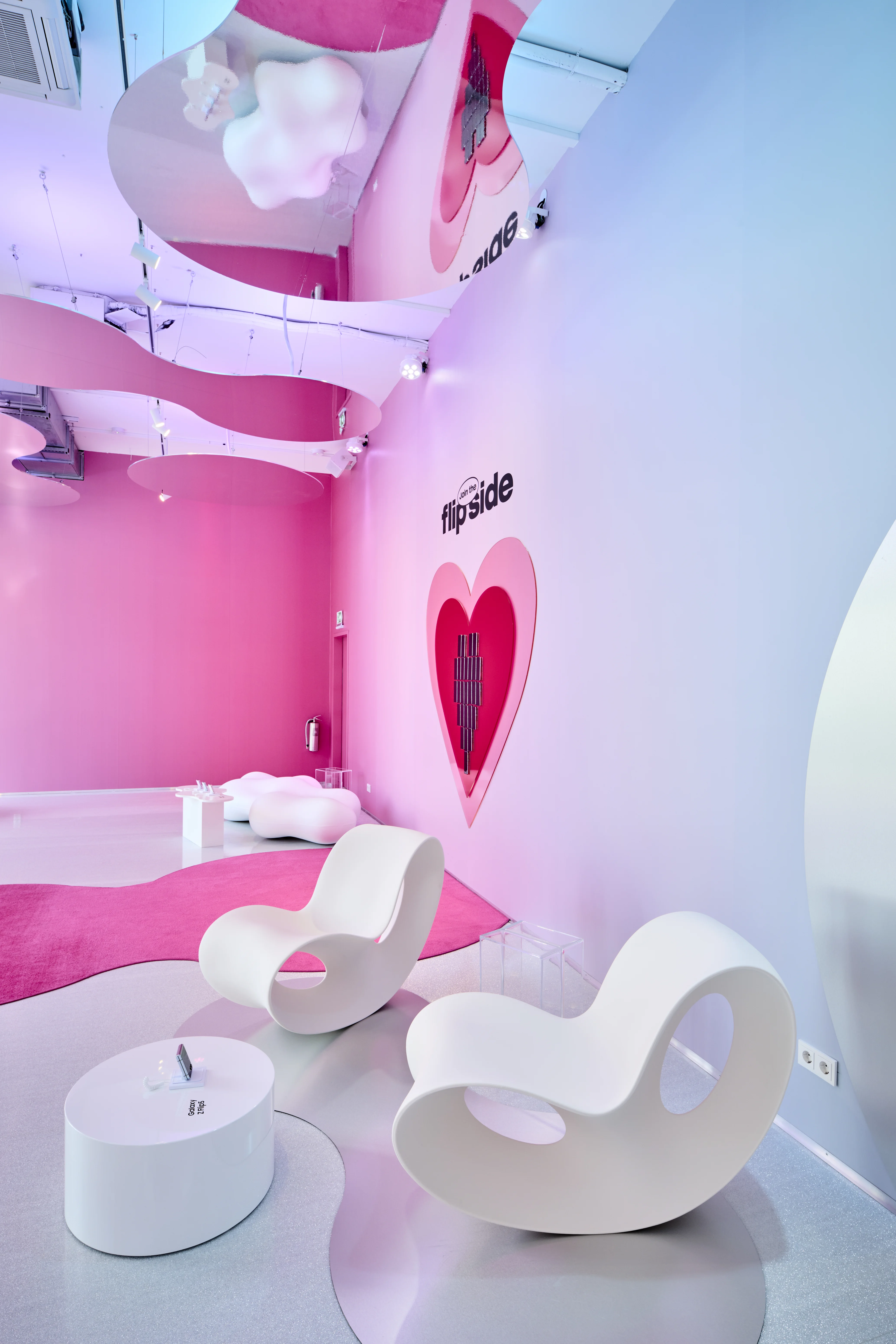 White rocking chairs and round side table in front of the pink Flipside heart wall at the Highsnobiety x Samsung pop-up.