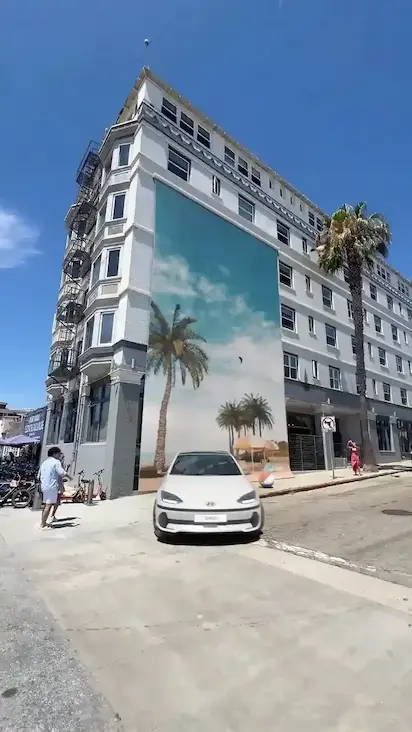 A white Hyundai car in front of a massive beach-themed mural on a city building
