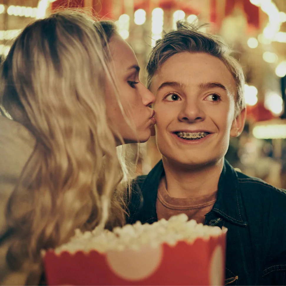 Kvinna kysser en ung man på kinden medan han håller en popcornbägare