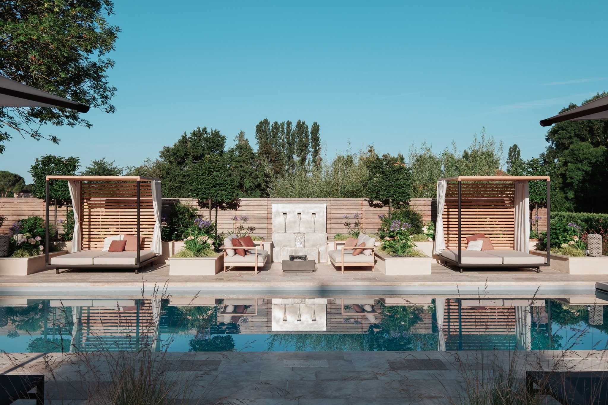 Aménagement extérieur avec piscine, lits de jardin et mobilier design entourés de verdure, reflétant harmonie, nature, sérénité et élégance selon la philosophie de conception d'Invivo Paysage