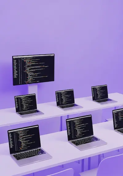 A modern classroom setup features multiple laptops displaying lines of code on a purple background, symbolizing software engineering and coding education.