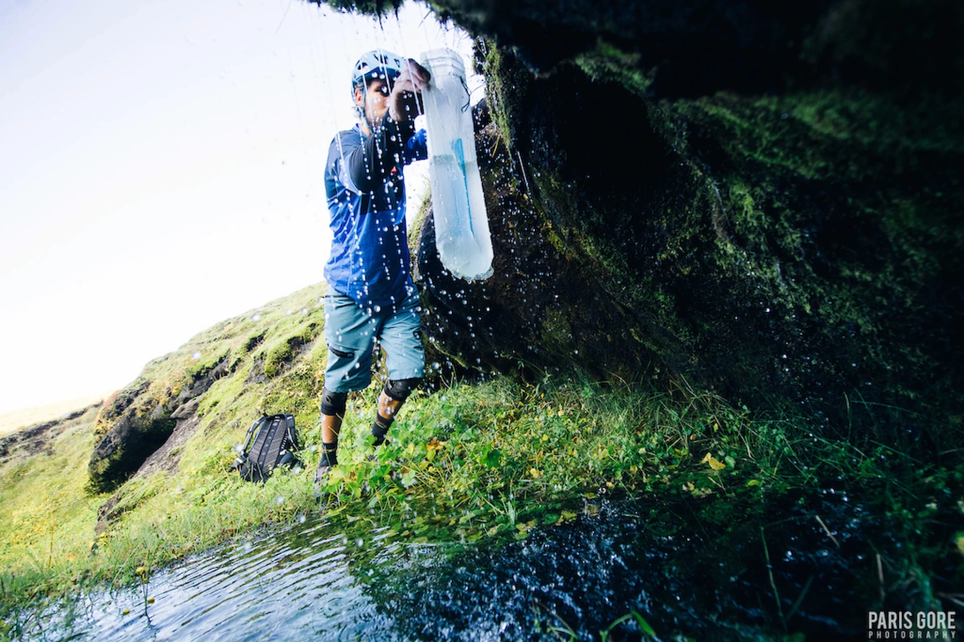 Man fills water bottle from a small stream