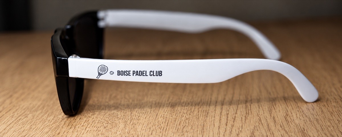 Boise Padel Club branded sunglasses on a wooden table