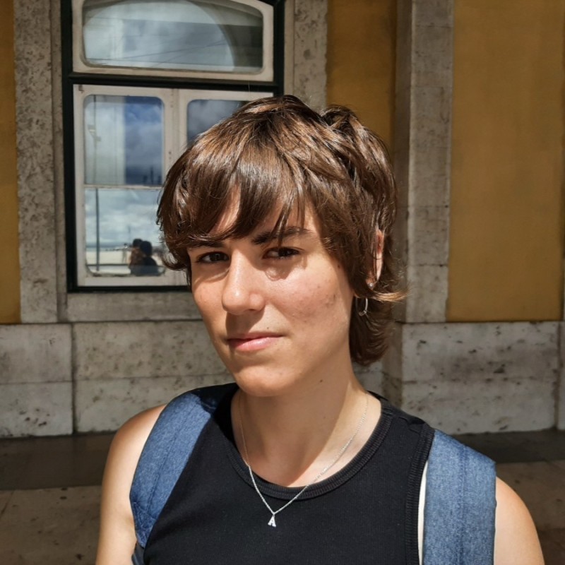 Donna con i capelli corti davanti a un muro giallo e una finestra.