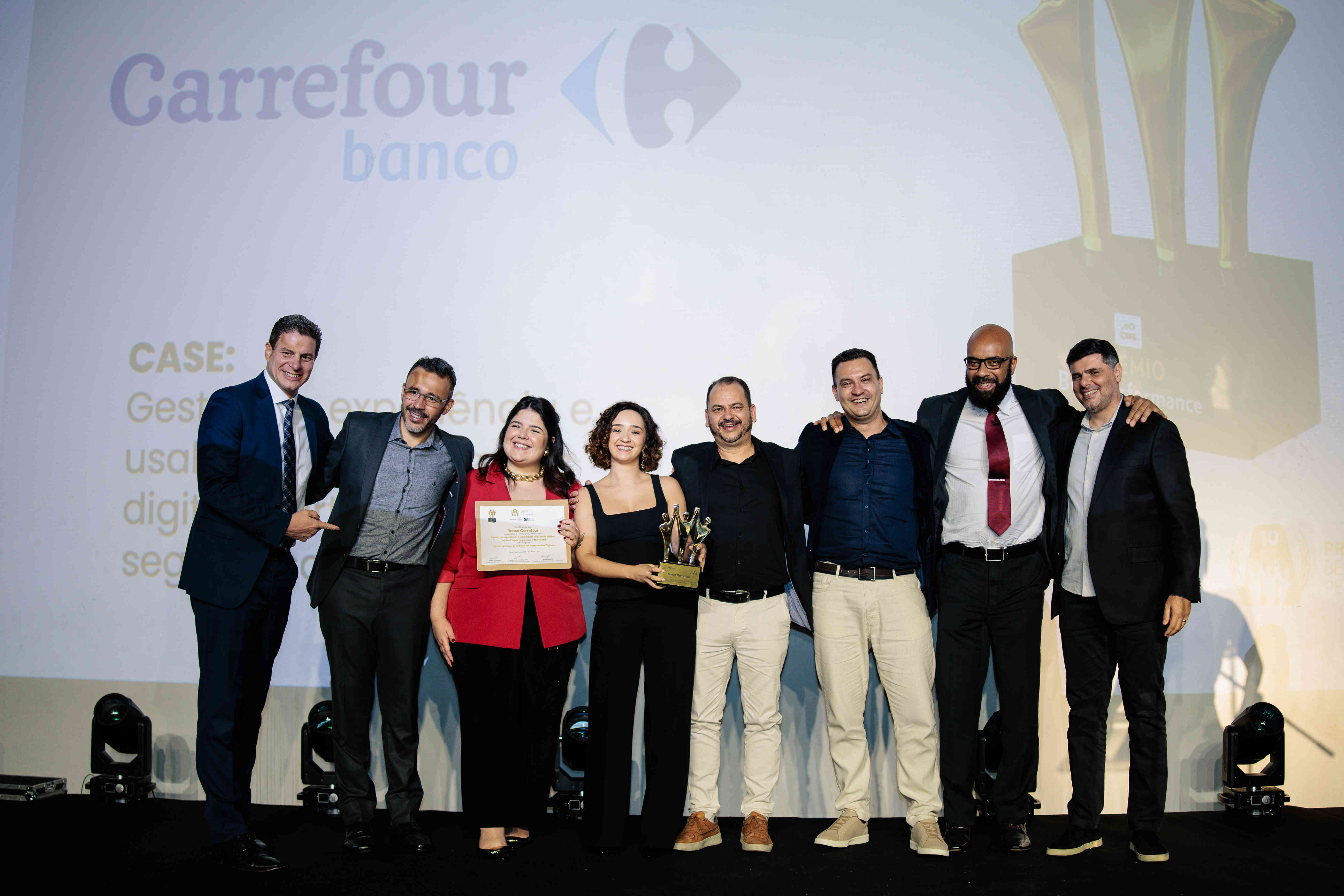 Executivos do Banco Carrefour posando com troféu ouro e certificado no palco do Prêmio Best Performance 2025