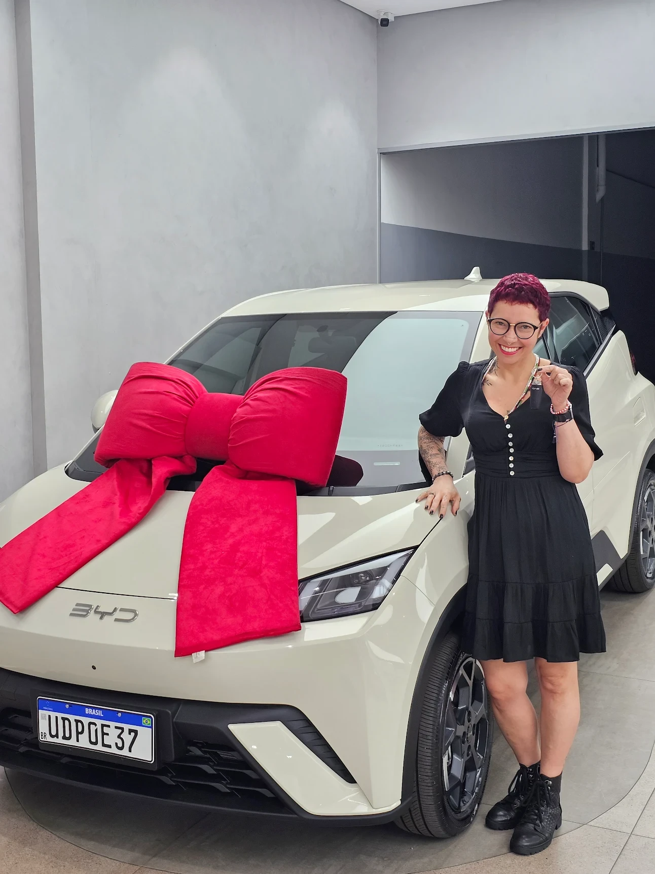 Anna Rachel Algazi, cliente Klubi, sorrindo ao lado do seu carro novo com laço vermelho no momento da entrega do consórcio contemplado.