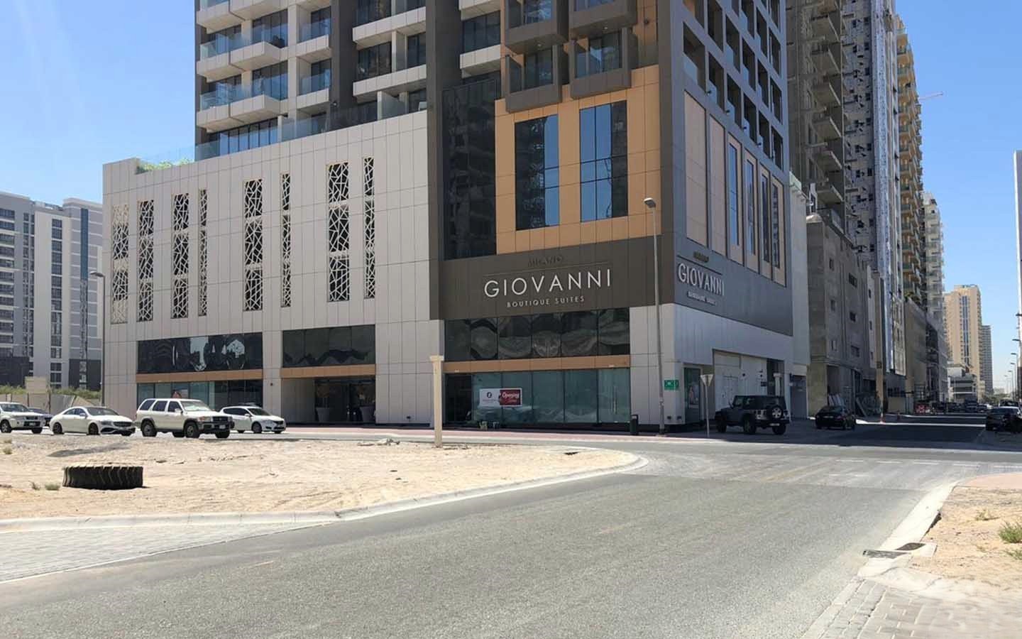 Street scene in Jumeirah Village Circle showing low-rise buildings and a distinctive, tall, cylindrical residential tower in the background.