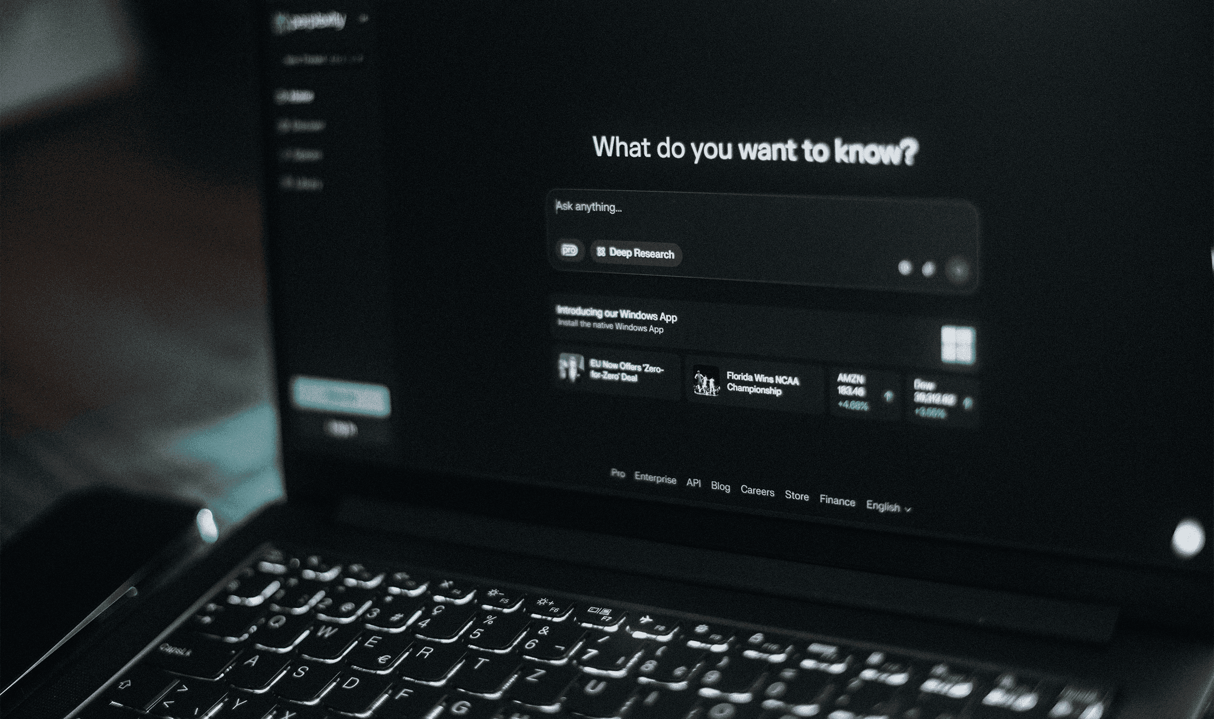A laptop in a dark room showing an AI search interface with an empty prompt field.