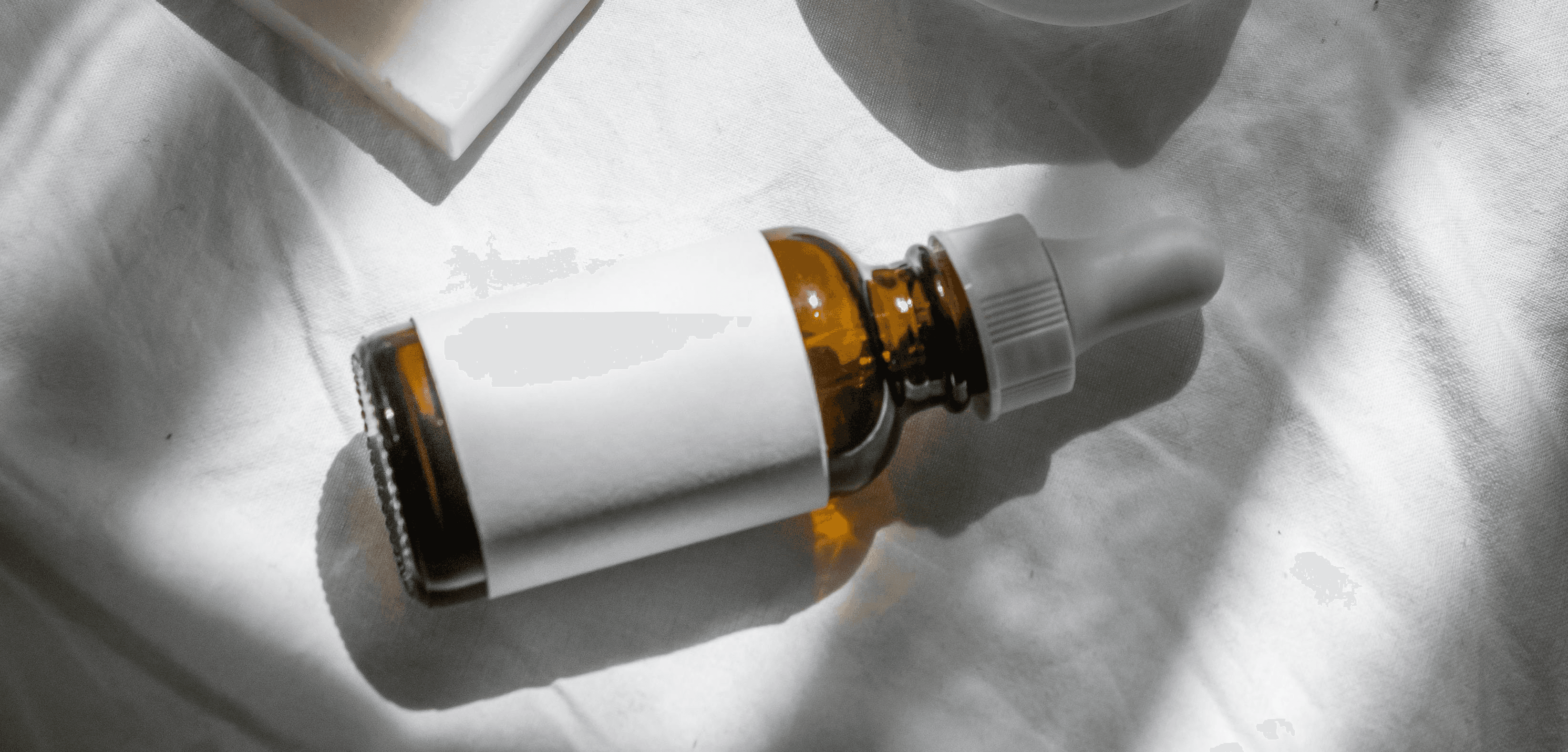 Brown dropper bottle with blank label. Skincare product bottle in sunlight. Beauty product aesthetic. Natural essential oils. Cosmetic branding.