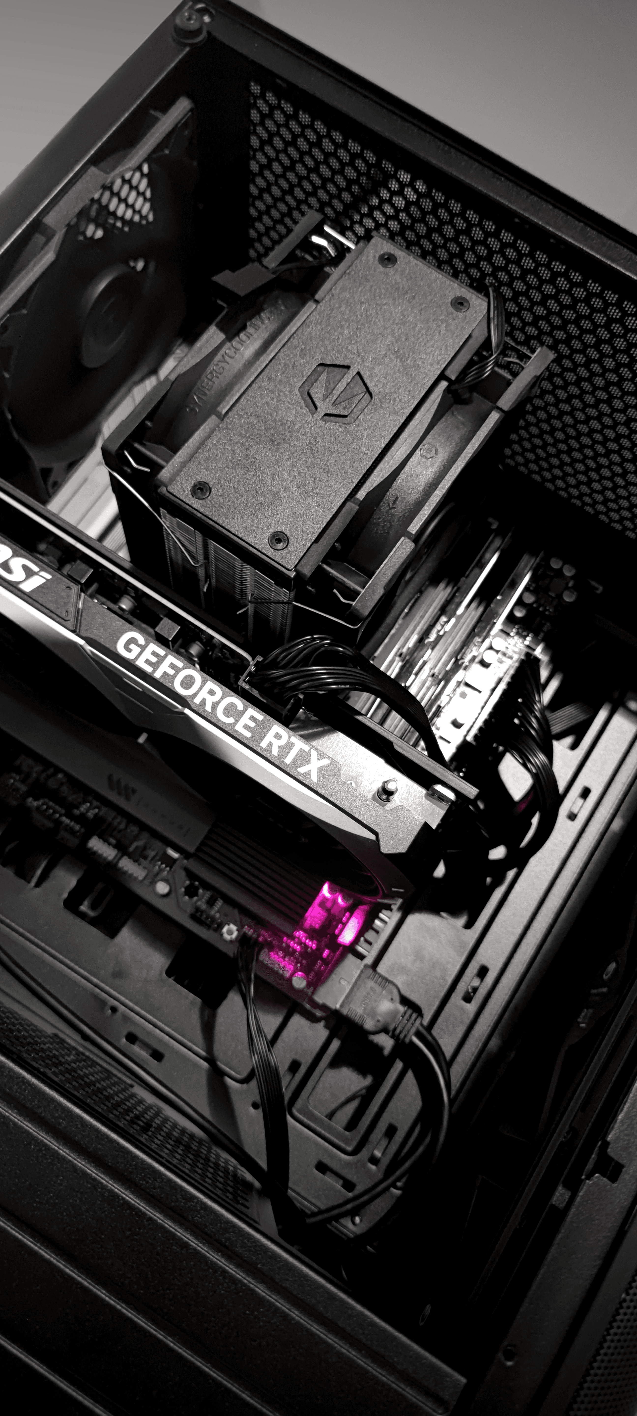 Czarno-białe zdjęcie wnętrza komputera z góry, przedstawiające kartę graficzną GeForce RTX oraz chłodzenie Endorfy; pod kartą widoczne jest punktowe, fioletowo-różowe podświetlenie LED.