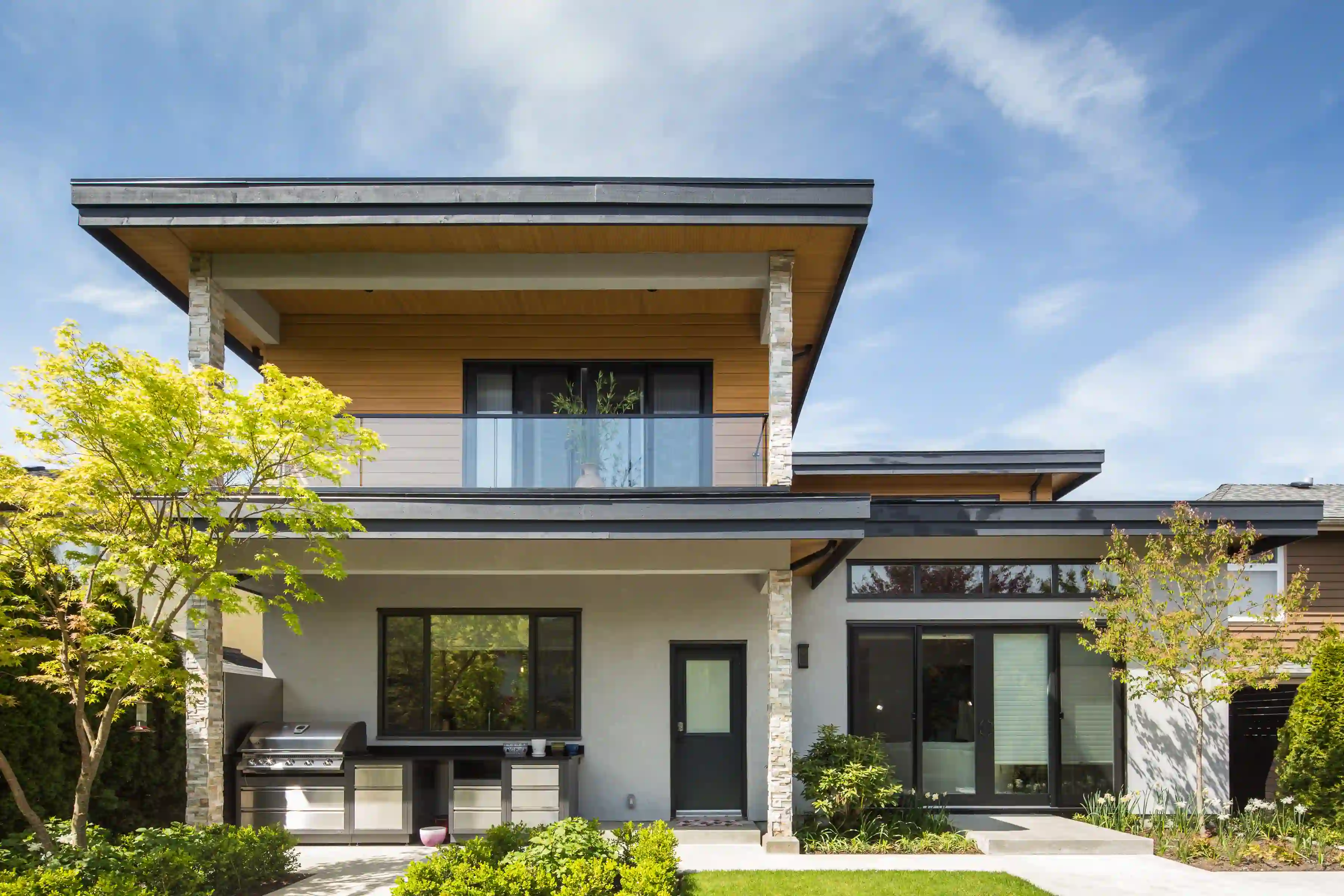 Modern custom home exterior with covered patio, balcony, and landscaped yard