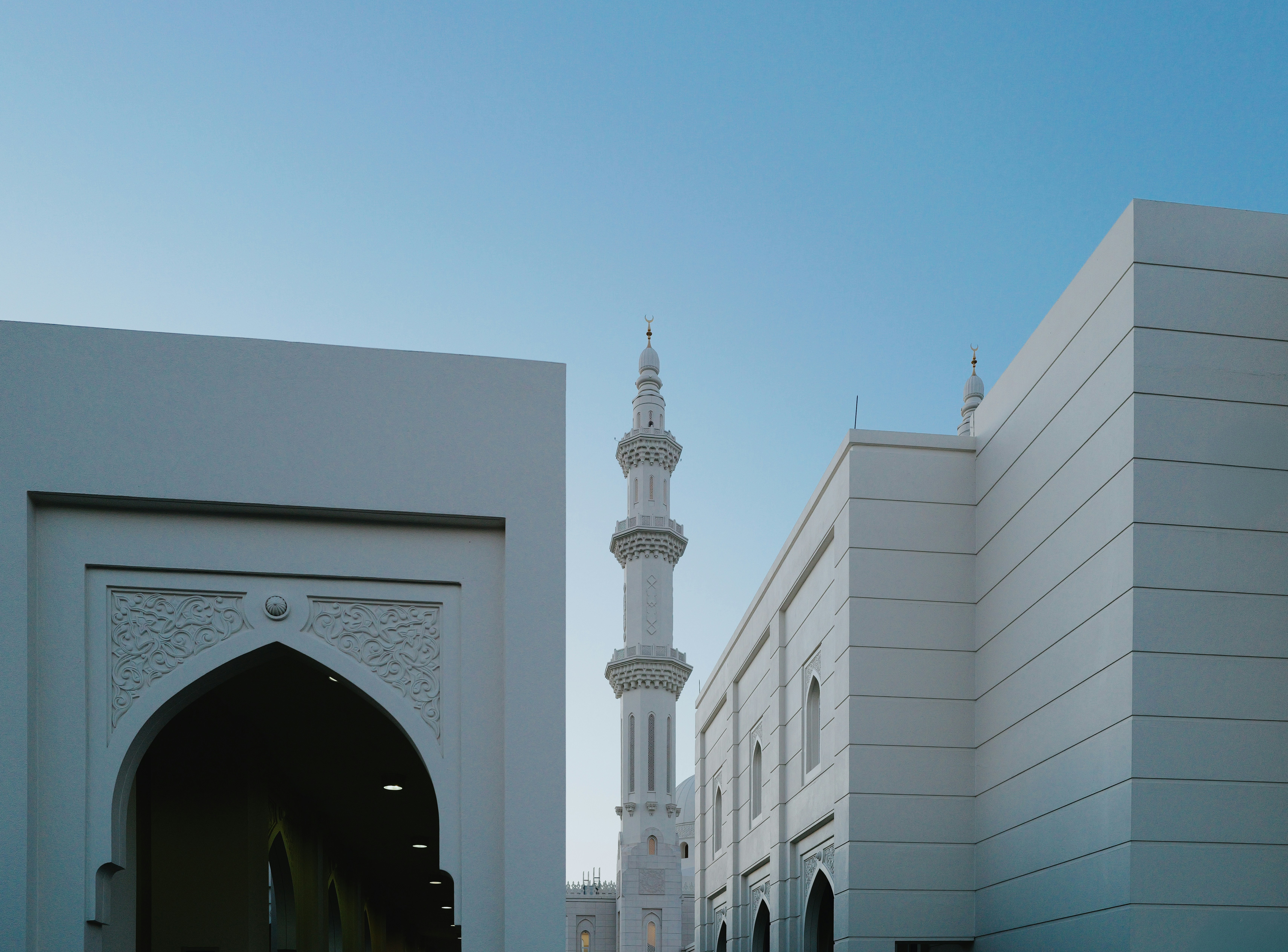 White mosque with minaret against blue sky.