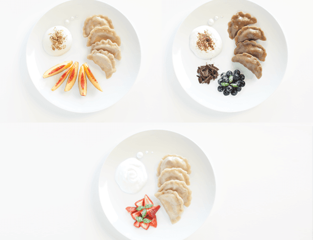 Three white plates are arranged on a white surface, each containing different food items. The top left plate holds thin, folded, light brown pastries, a small dollop of white cream, a sprinkle of brown powder, and a few thin, curved, light brown pieces. The top right plate contains small, round, dark blue berries, a small pile of dark brown crumbles, and a small dollop of white cream. The bottom plate holds several folded, light brown pastries, a small dollop of white cream, a small pile of red and orange pieces, and a small white swirl.