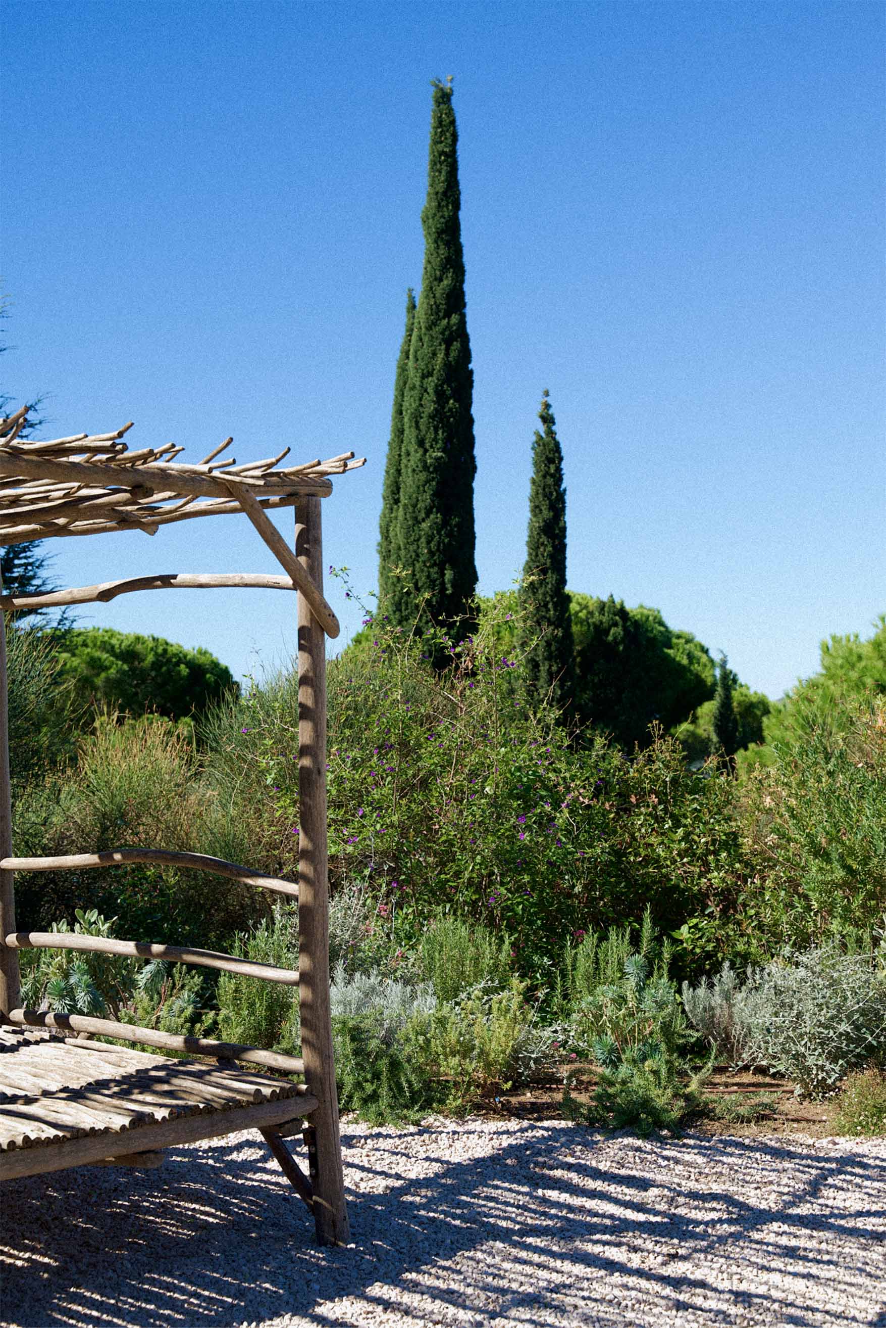 A black wooden house with a sloped roof and white door sits amidst tall, dry grass under a clear blue sky, conveying a peaceful rural setting.