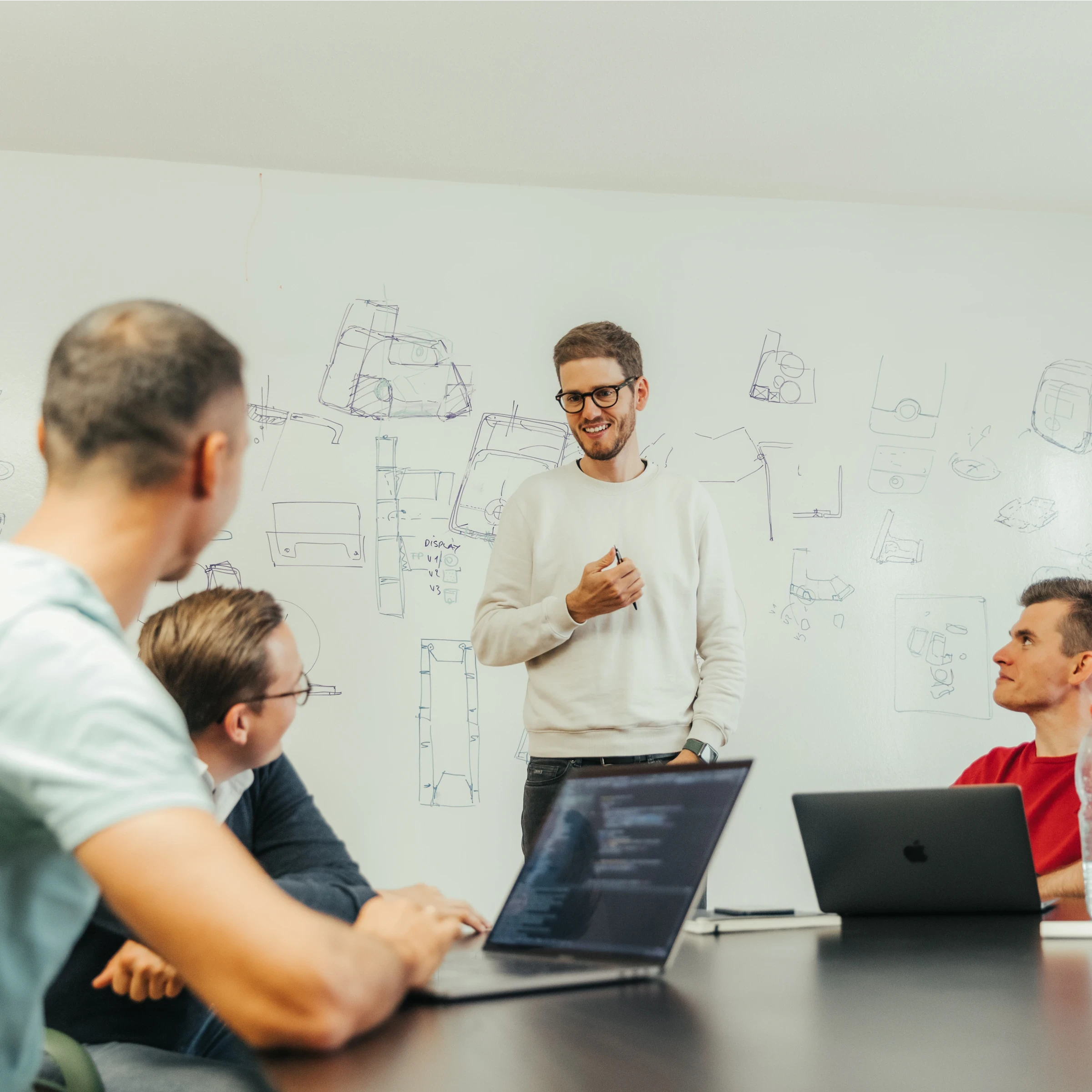 Designer presenting concept sketches to team with laptops, explaining innovative product designs in collaborative meeting.