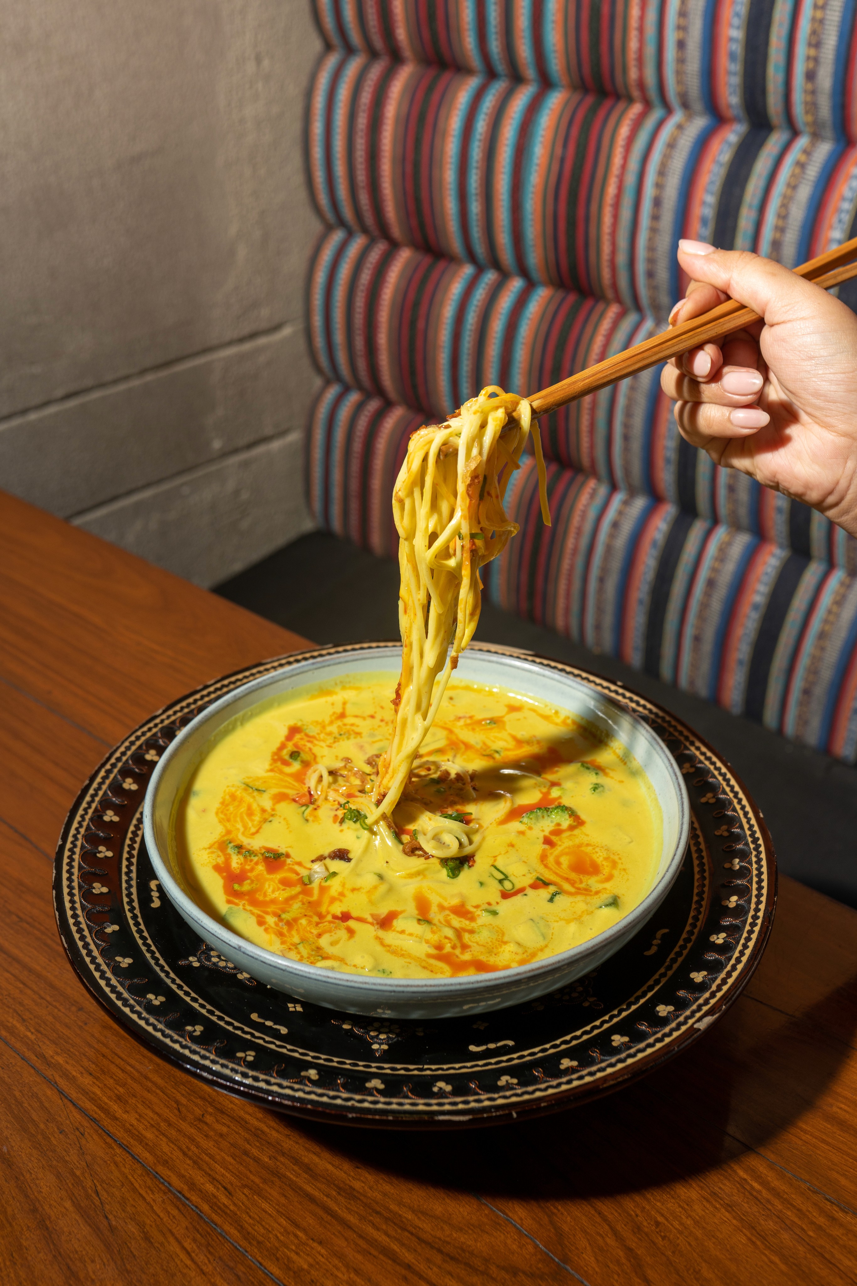 Bowl of Khow suey noodles lifted with chopsticks