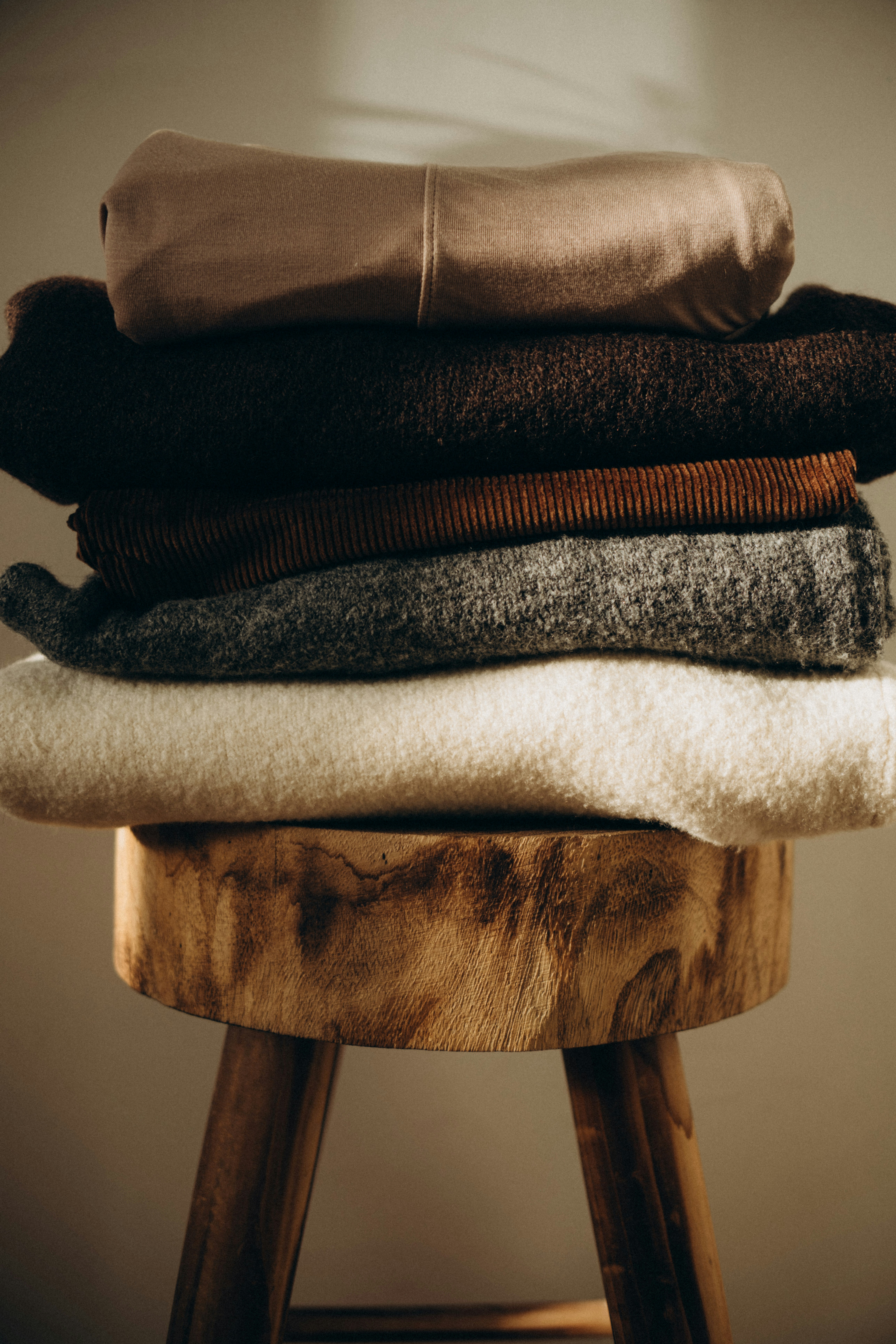 Folded knit sweaters stacked on a wooden stool