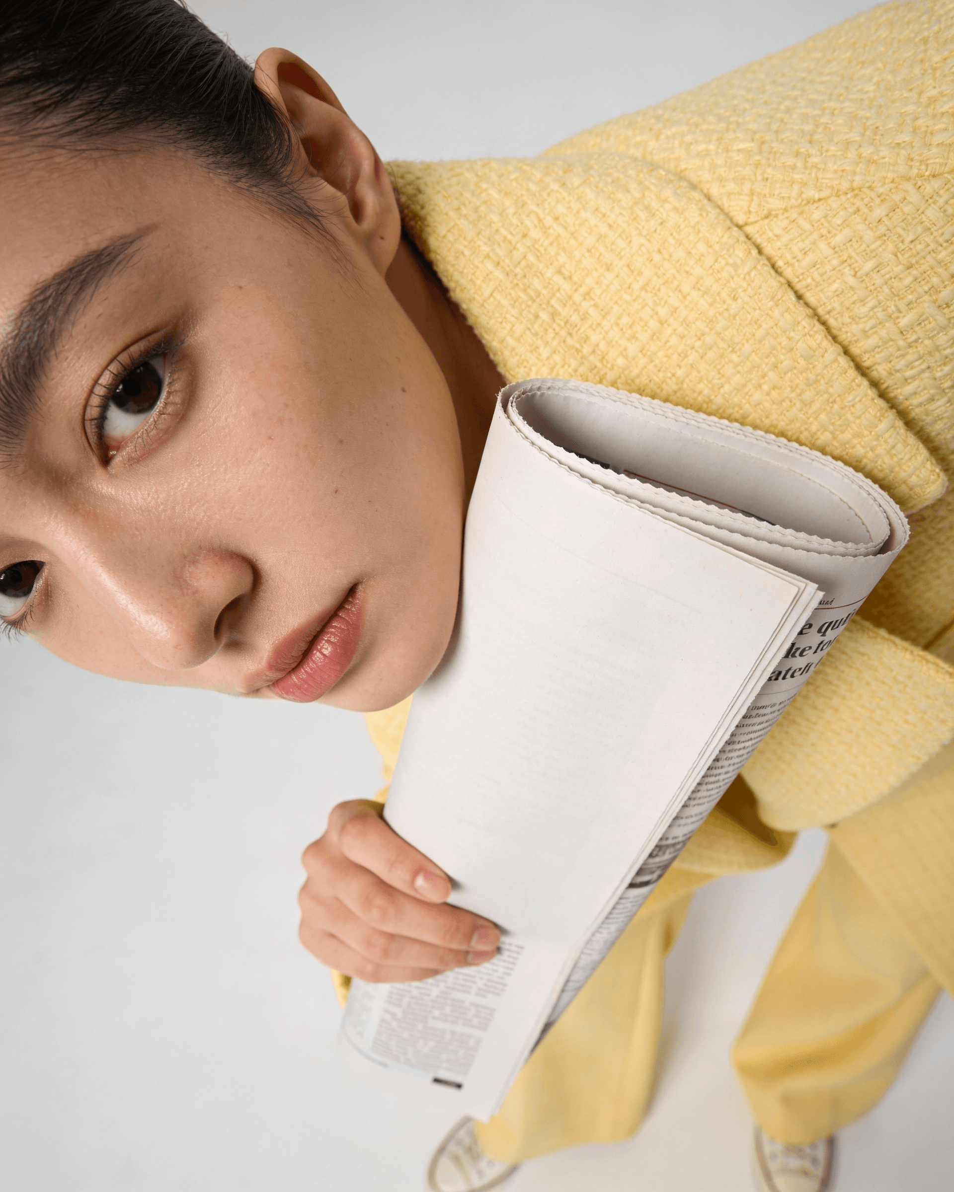 Close-up of a person holding a rolled-up newspaper, wearing a yellow outfit