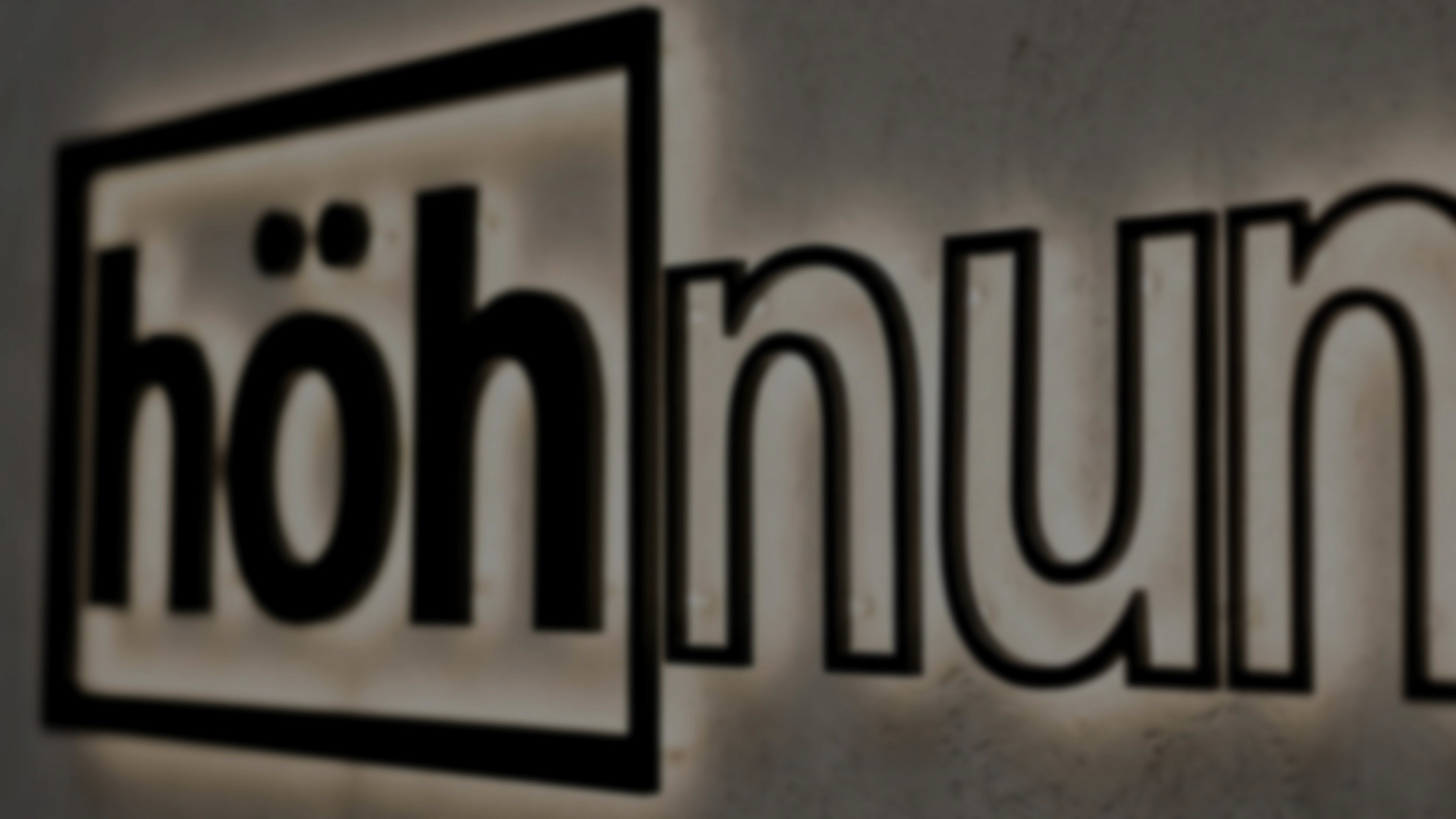 A man stands while two people sit at a table in an office setting, smiling and engaged in conversation. The mood is friendly and collaborative.