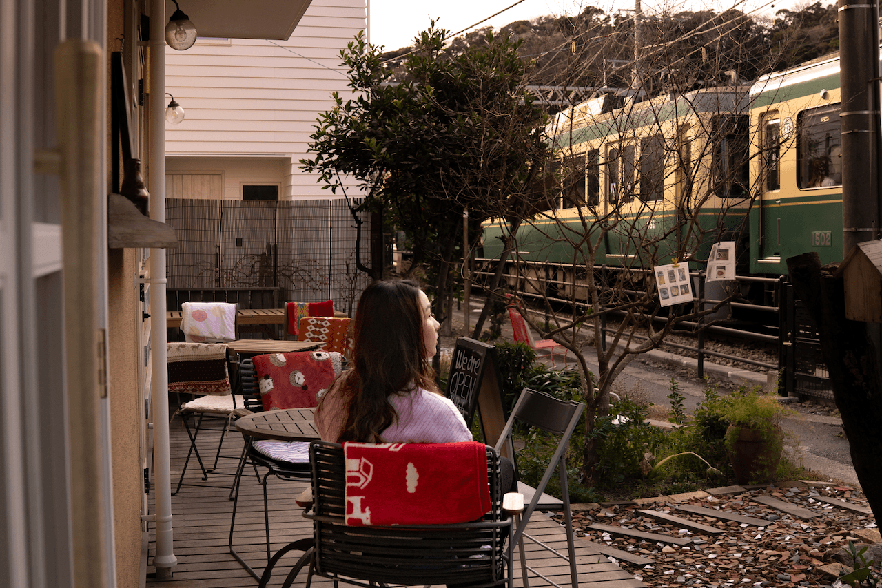 Person sitting on the terrace of Cafe Umi no Tonari watching a train go past