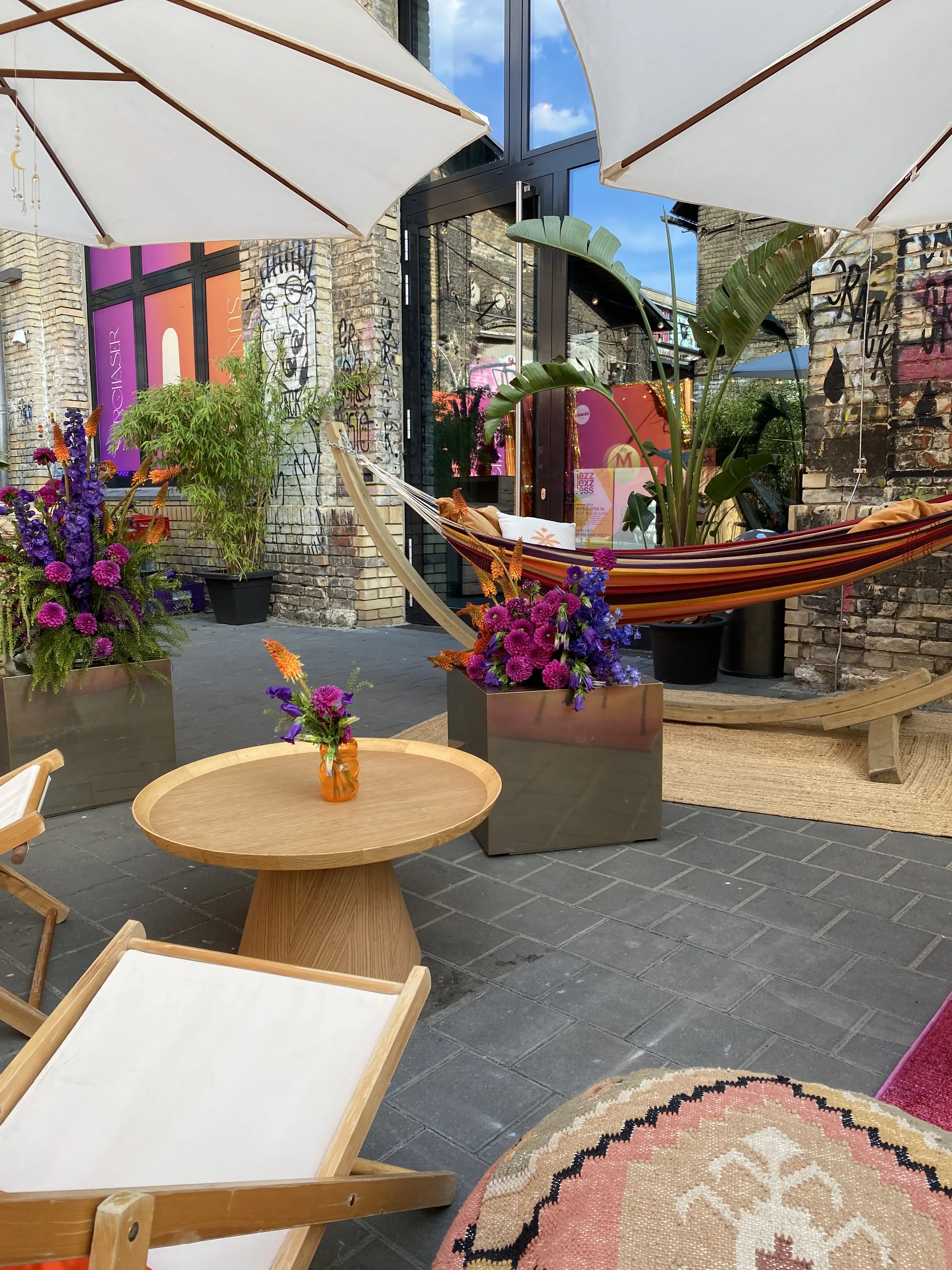 Striped hammock on wooden stand next to flower boxes and round wooden table in the courtyard.